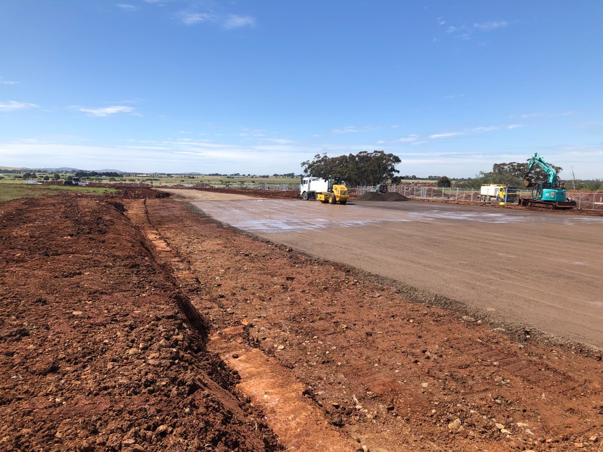 Aintree Specialist School (interim name) - construction photo of site progress in December 2022 - red dirt paddock with a truck and a digger in the background