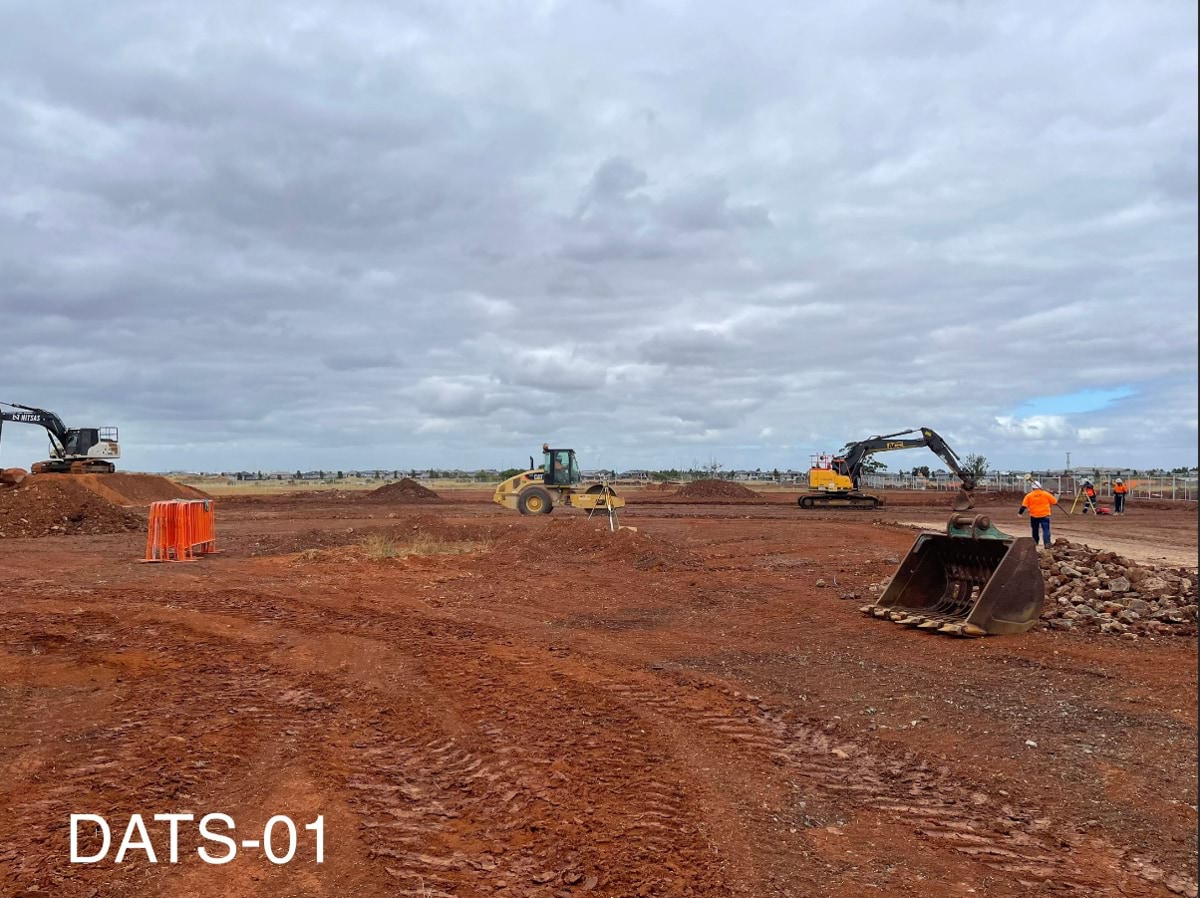 Aintree Secondary School (interim name) - construction photo of site progress in January 2023 - red dirt paddock with 2 cranes, a digger and a worker in high-vis.