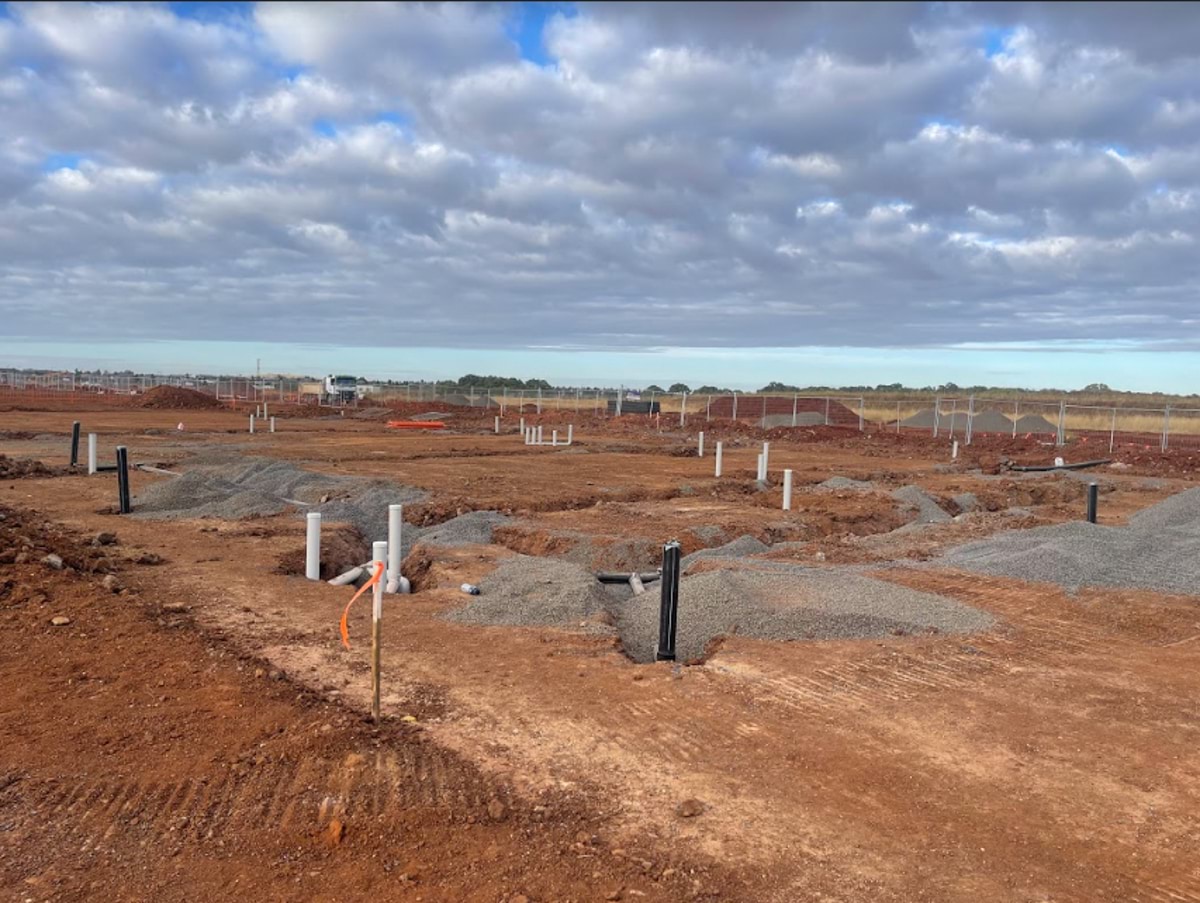 Aintree Secondary School (interim name) - construction photo of site progress in February 2023 - excavation intro red dirt paddock with trenches and white tubing