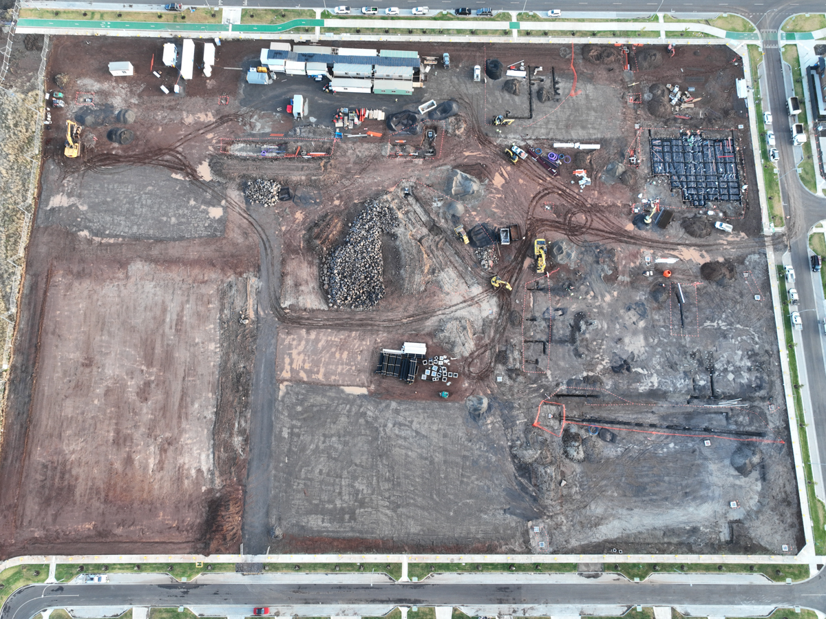 Tarneit North Primary School (interim name) - construction photo of site progress in February 2023 - aerial shot of site surrounded by access roads on 3 sides, flattened dark earth, construction vehicles and portables