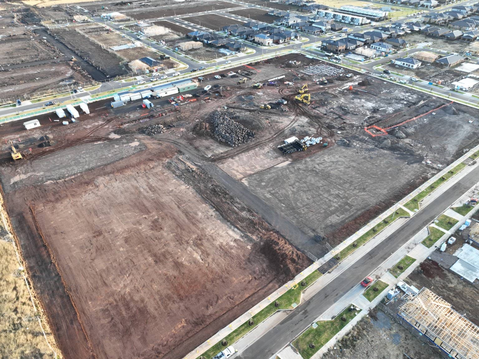 Tarneit North Primary School (interim name) - construction photo of site progress in February 2023 - aerial shot of site surrounded by access roads on 3 sides, flattened dark earth, construction vehicles and portables