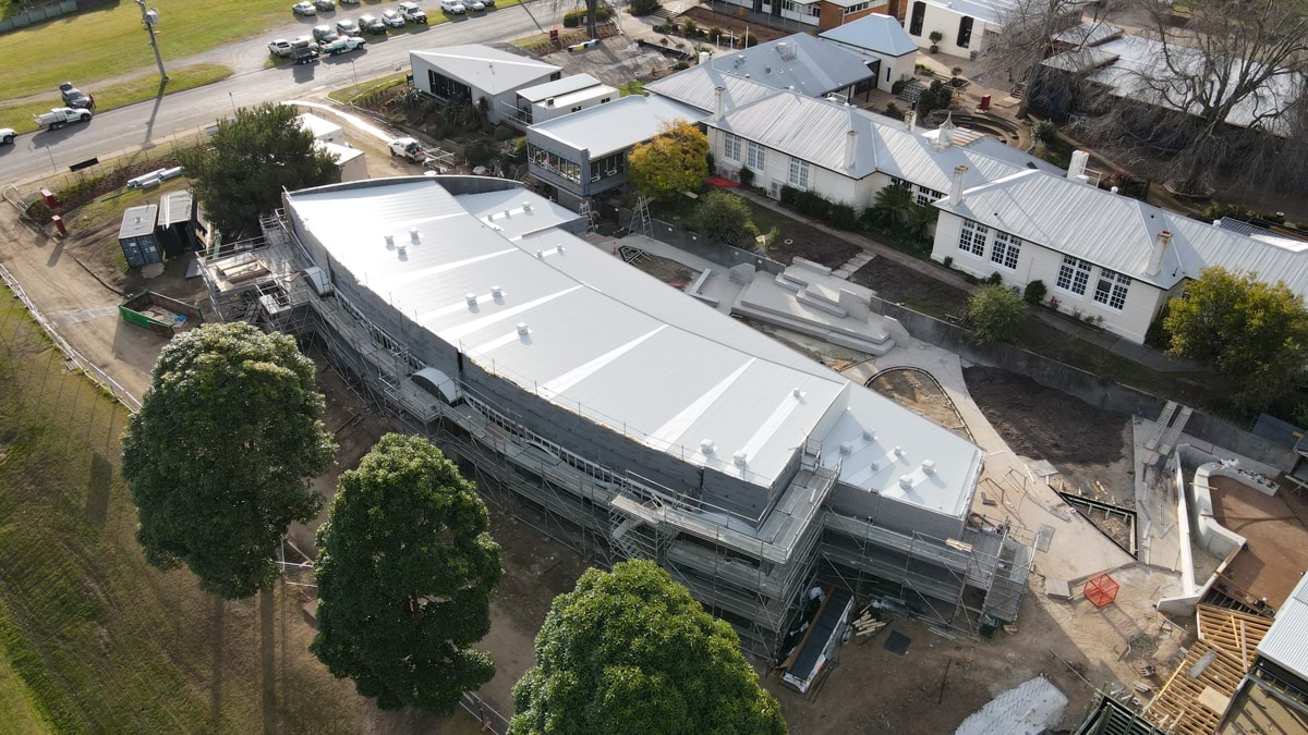 This is an aerial image of the Orbost Community College construction site. It shows the exterior of a new school building amongst existing school buildings, surrounding trees and road access.