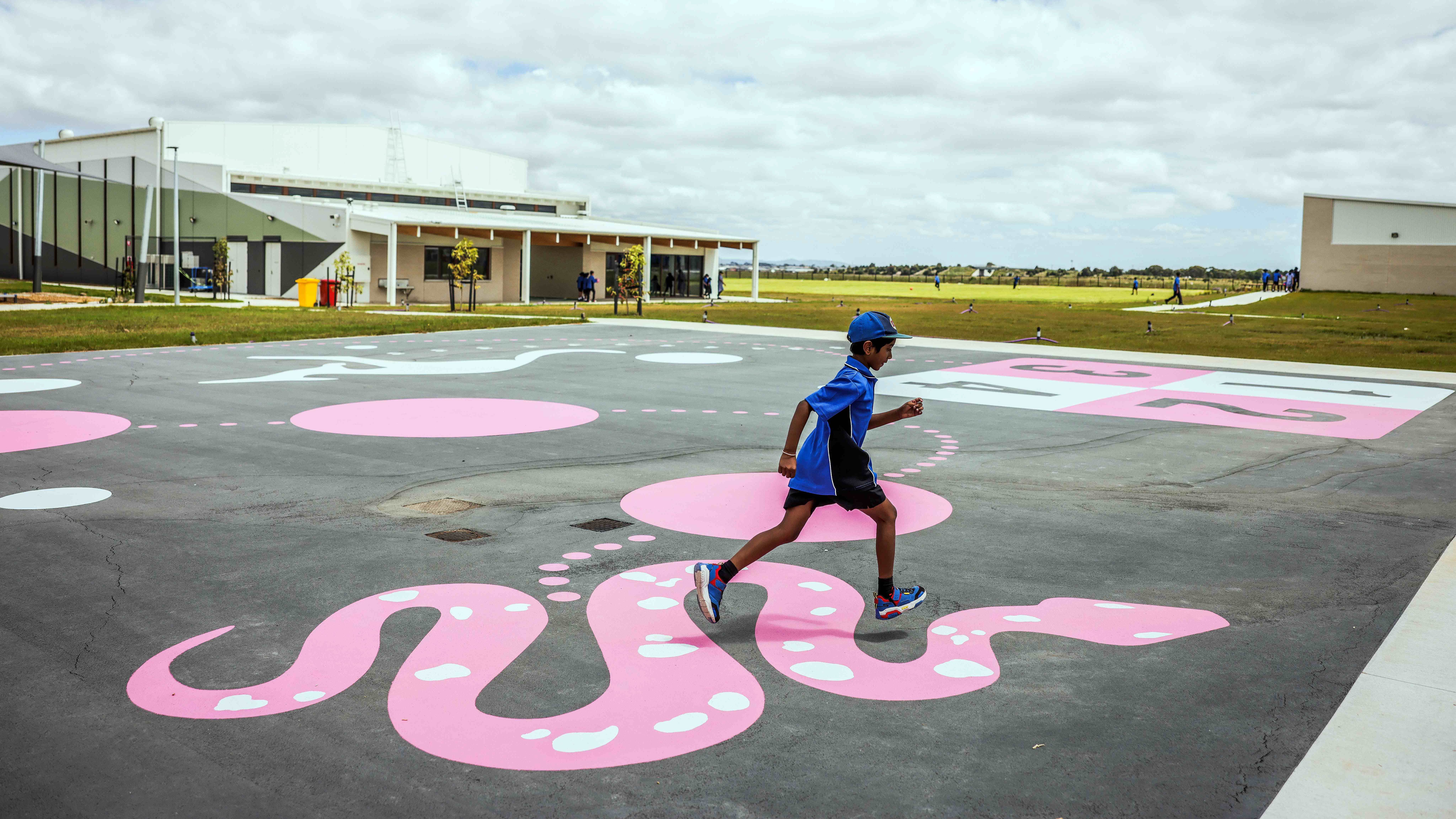 young boy on an outdoor play area, jumping across a painting of a pink serpent