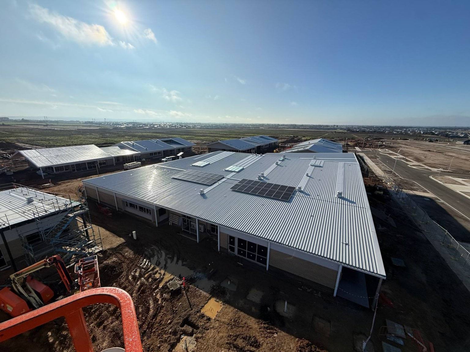 View of the top of constructed buildings with solar panels visible. Buildings are situated in muddy paddock
