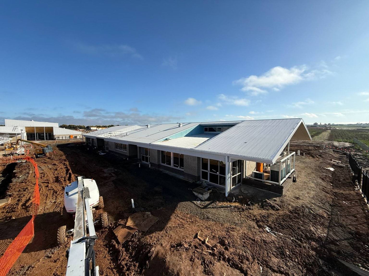 View of the top of constructed buildings with triangular shaped roof featured. Buildings are situated in muddy paddock