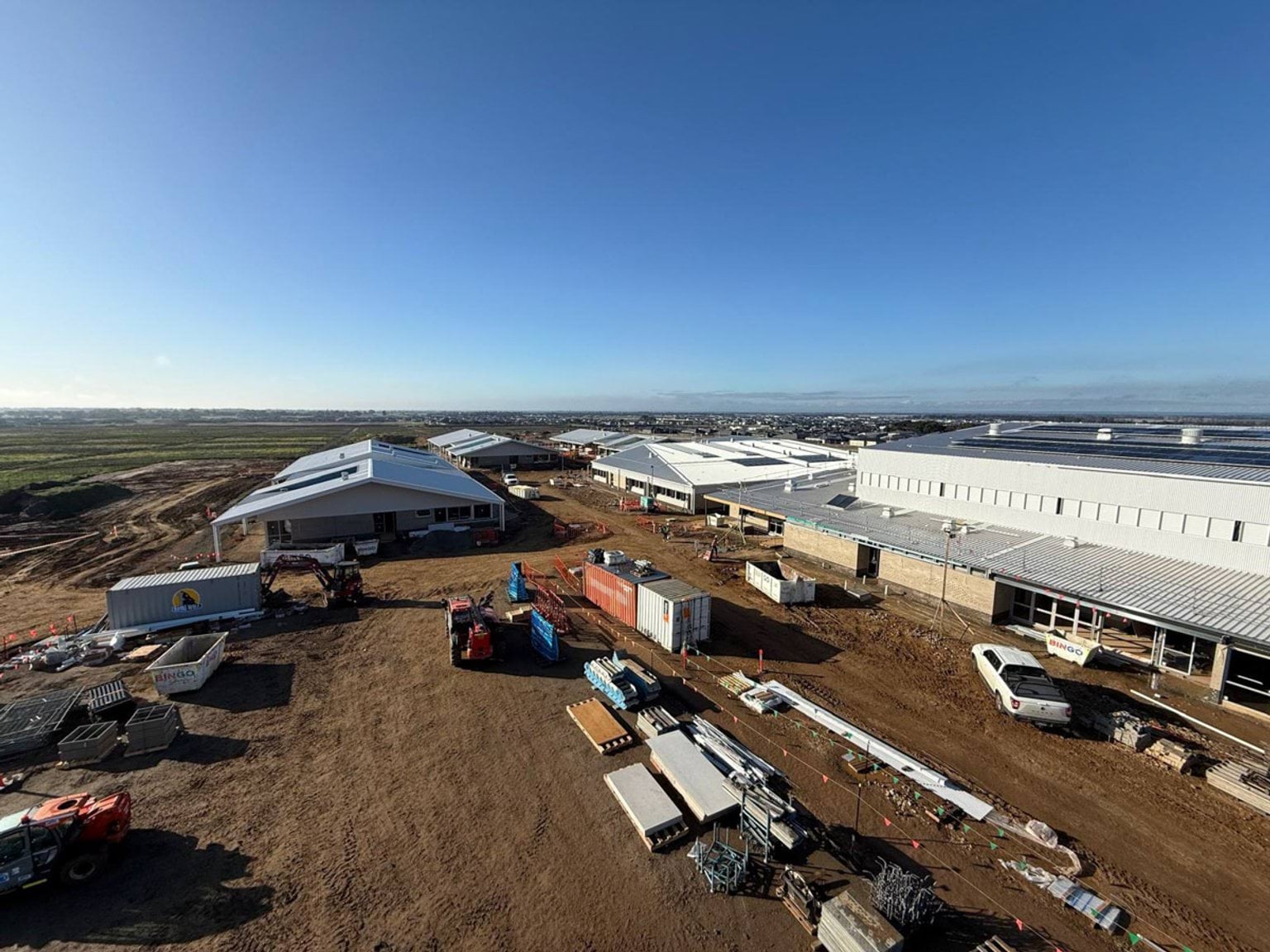 View of the top of constructed buildings with building supplies placed in courtyard. Buildings are situated in muddy paddock