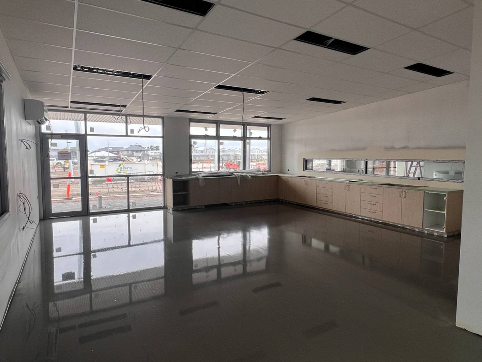 Classroom with new gloss varnished finish for floor reflecting light from windows. Electrics still need to be completed with cabling hanging from the ceiling.