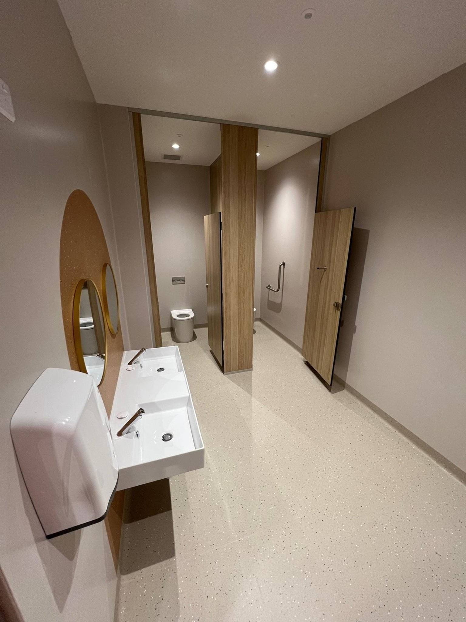 New double cubicle bathroom with timber doors, square porcelain sinks, and round mirrors.