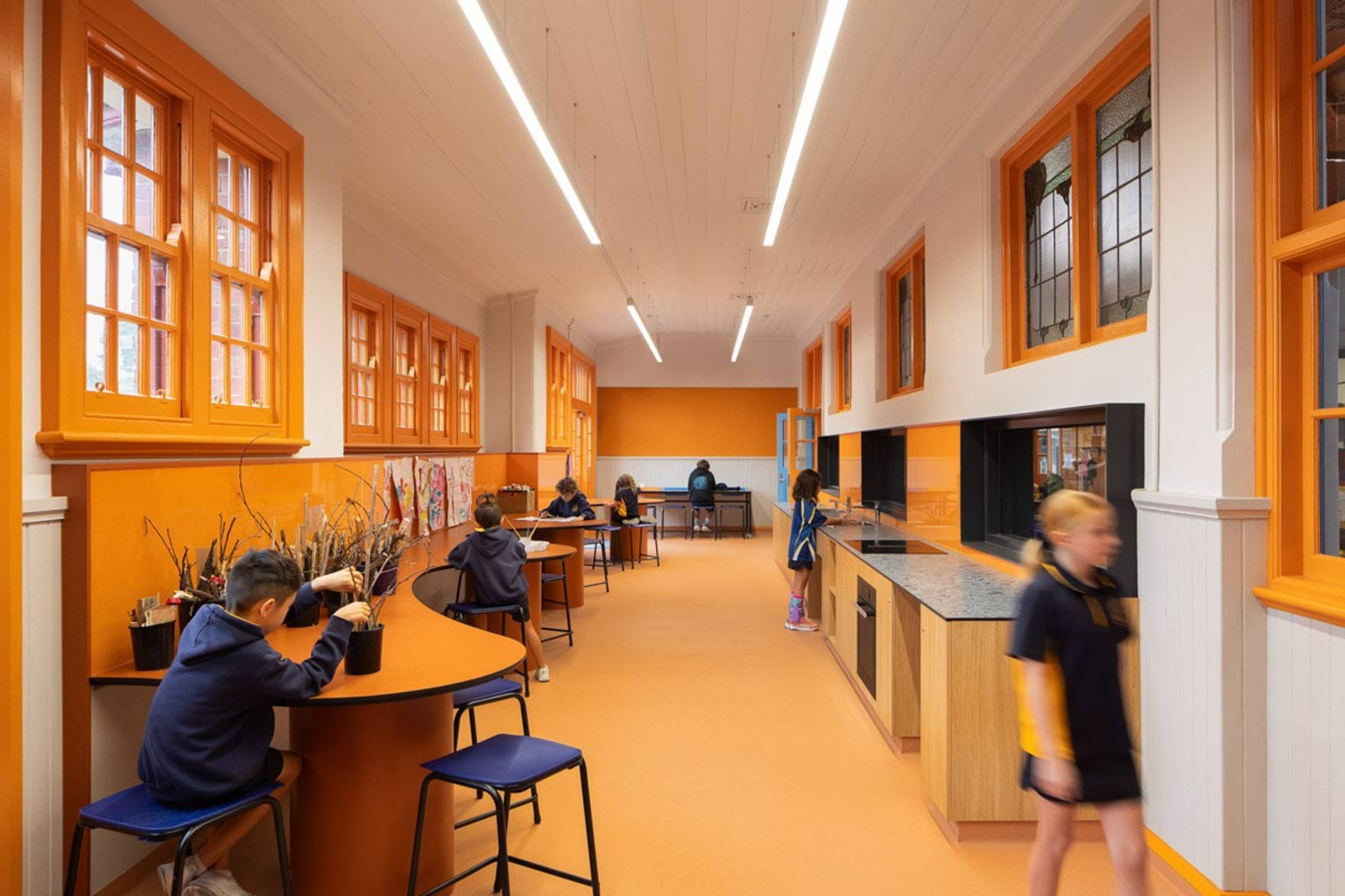Inside Moonee Ponds West Primary School. It's a long room with a yellow floor, yellow features on the walls, yellow window frames and yellow tables. Kids are sitting at the long wavy table against the wall, or using the sink on the other wall. 