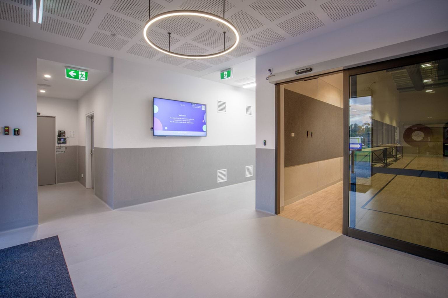 Indoor photo of room inside school building. There is a television on the wall, overhead lighting, and a hallway