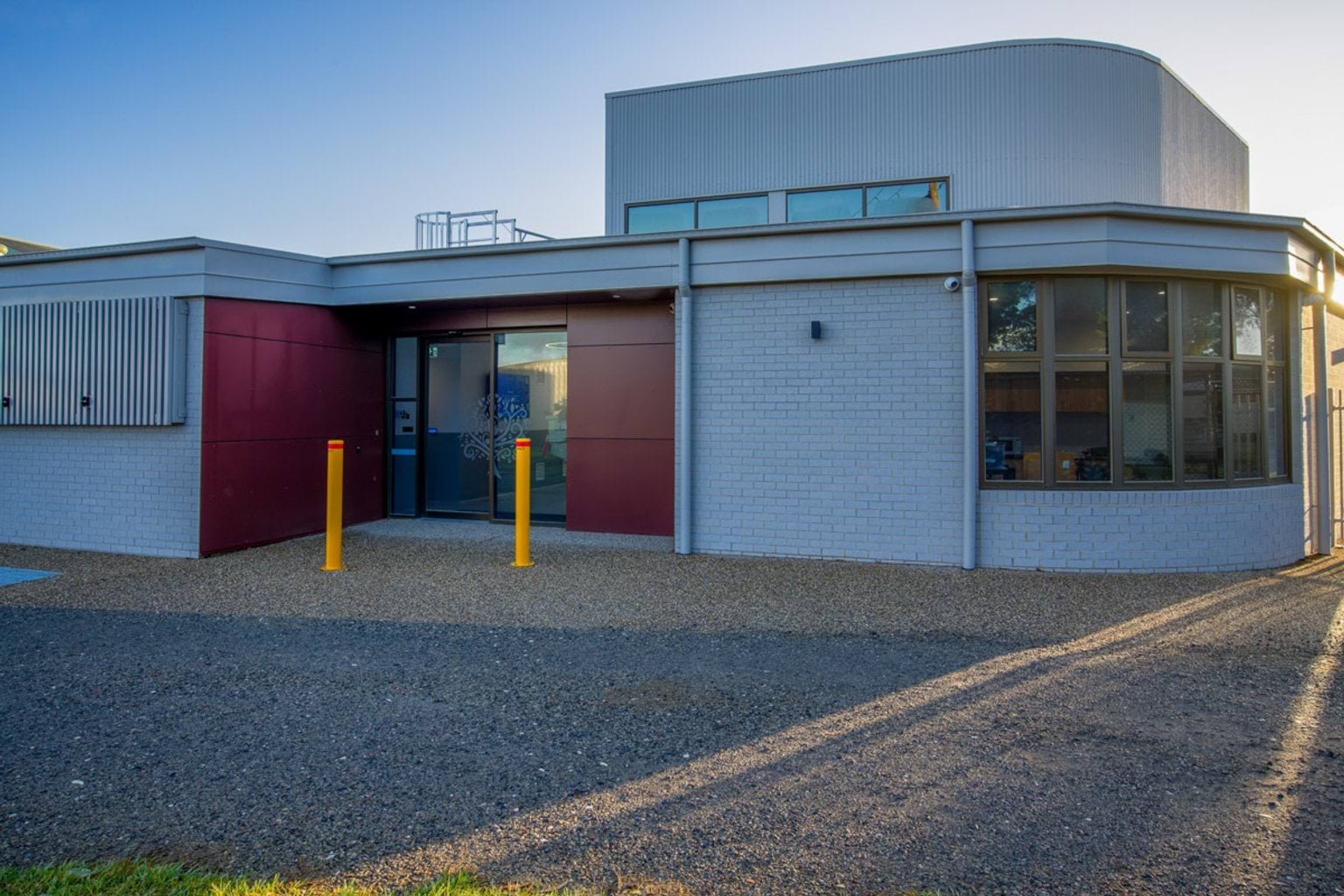 Outdoor photo of white brick school building with a red feature wall and glass door