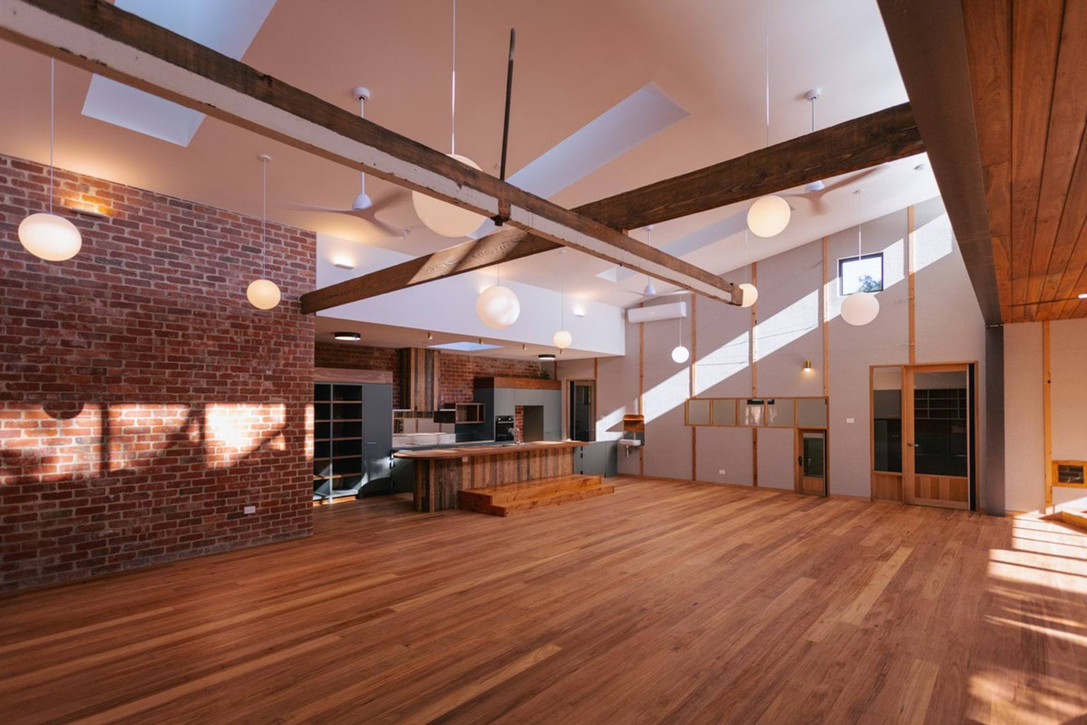 Inside a room of St Kilda & Balaclava Kindergarten. There is a brick wall and wooden floors. Round lights hang from the high ceiling. 