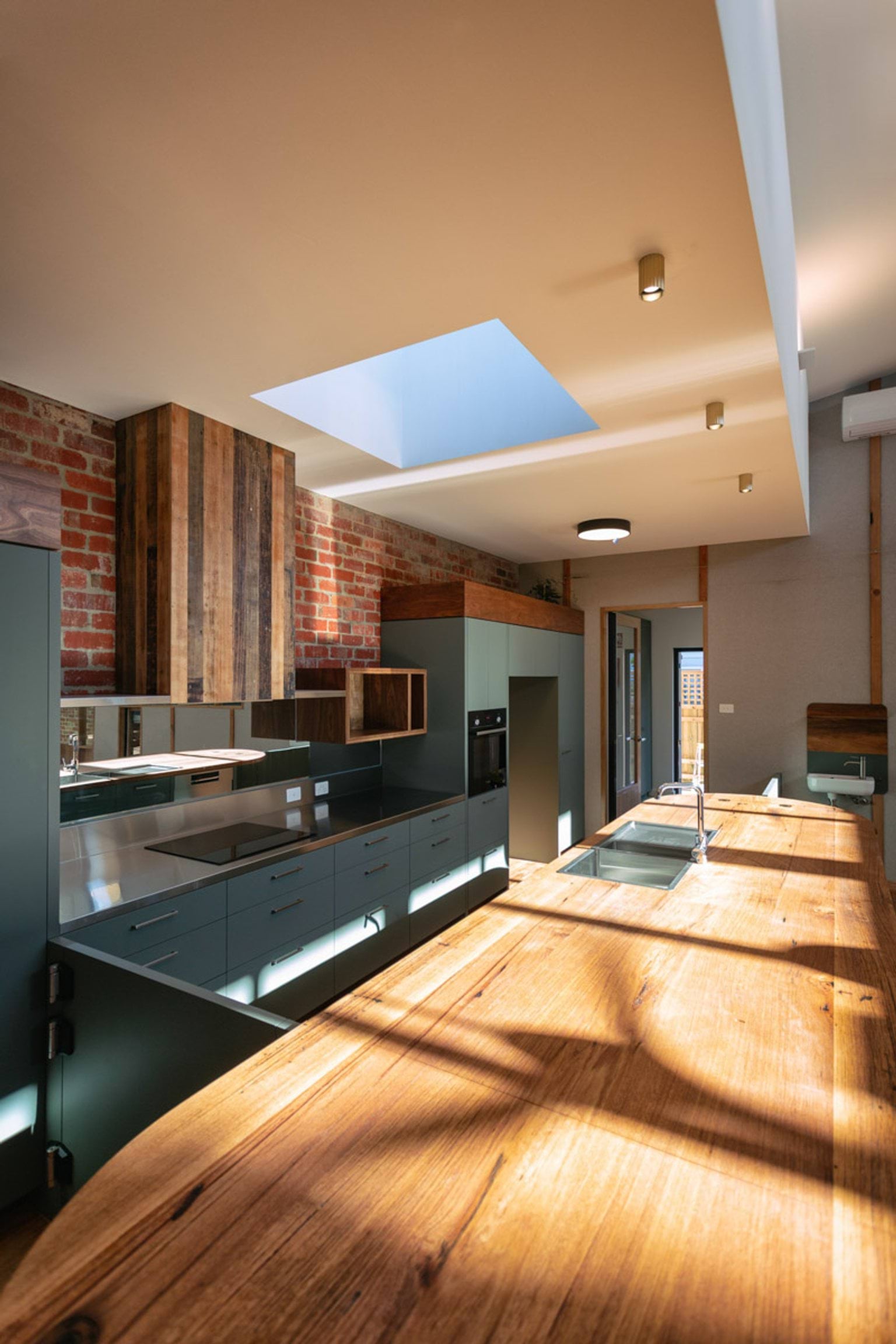 Inside the kitchen of St Kilda & Balaclava Kindergarten. The cupboards against the back wall are dark green and there is a long wooden bench in the middle. There is a skylight in the ceiling.