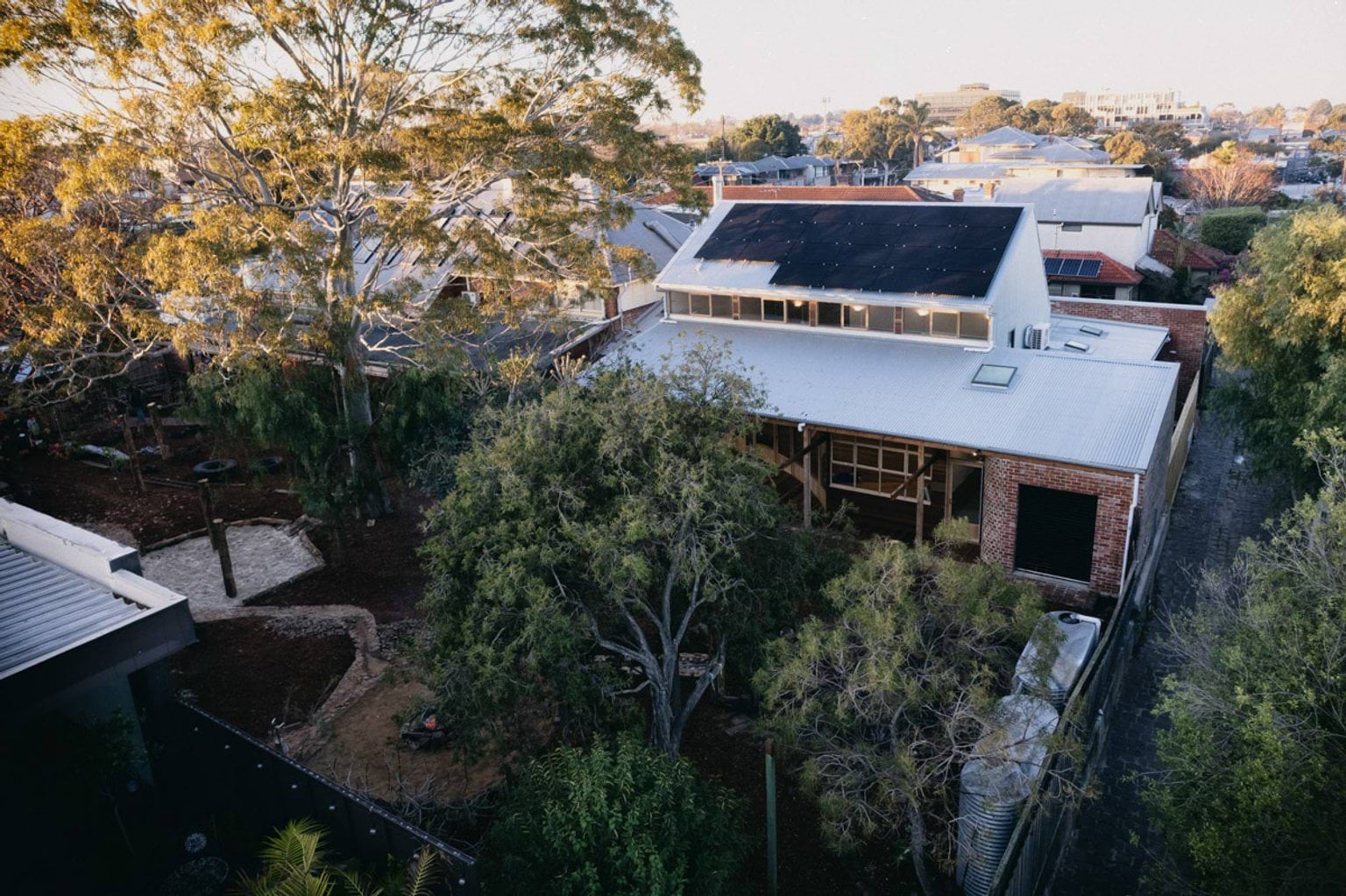 An aerial photo of the back of St Kilda & Balaclava Kindergarten, showing the outside area and its tall trees. The building has solar panels on the very top of the roof. 
