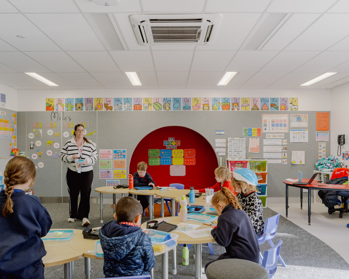 Inside a classroom of Swan Hill Specialist School with kids sitting at desks and a teacher standing. There are lots of colourful posters on the walls. 