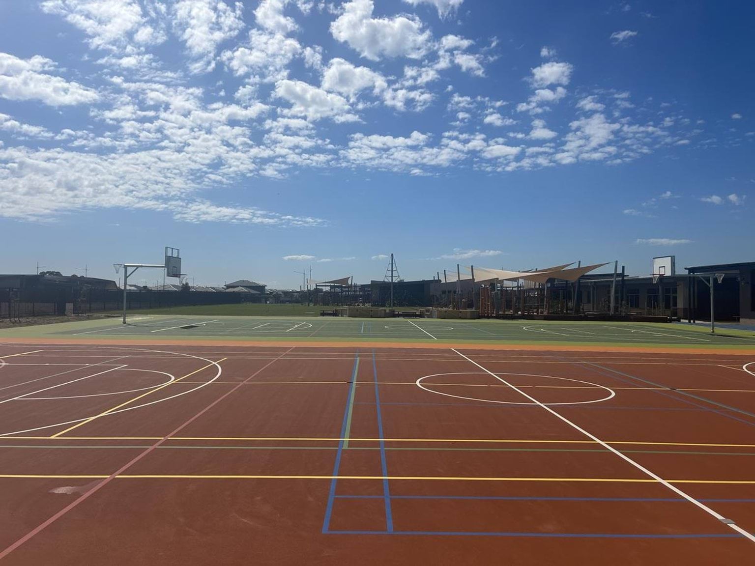 A photo of the new hard courts at Murrum Primary School. There is one orange and one green court. There are basketball hoops and line markings for various types of sports that can be played on the courts.