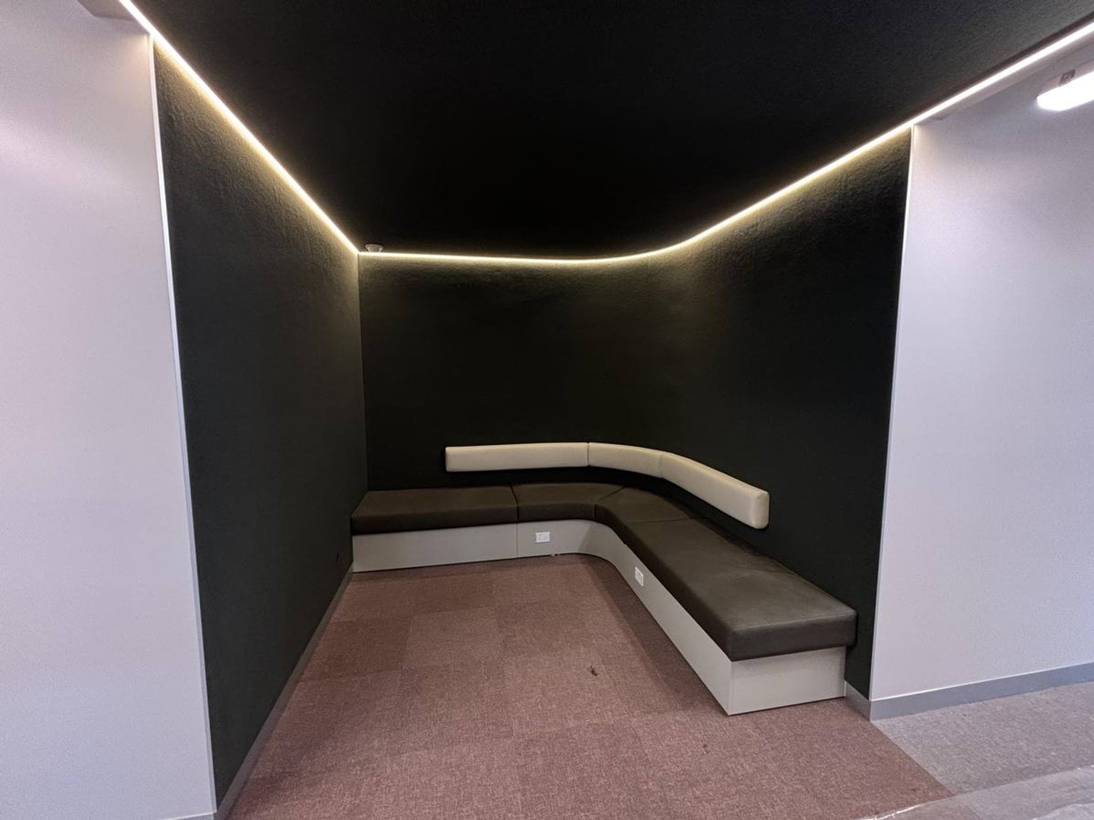 Inside one of the new buildings at Ngurraga School. The photo is of a corner that has dark walls, a bench seat wrapping around the corner and soft lighting running along the ceiling.