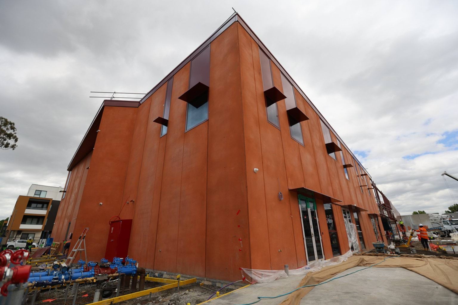 Multilevel school building under construction. It has orange walls and double doors with windows and scaffolding.