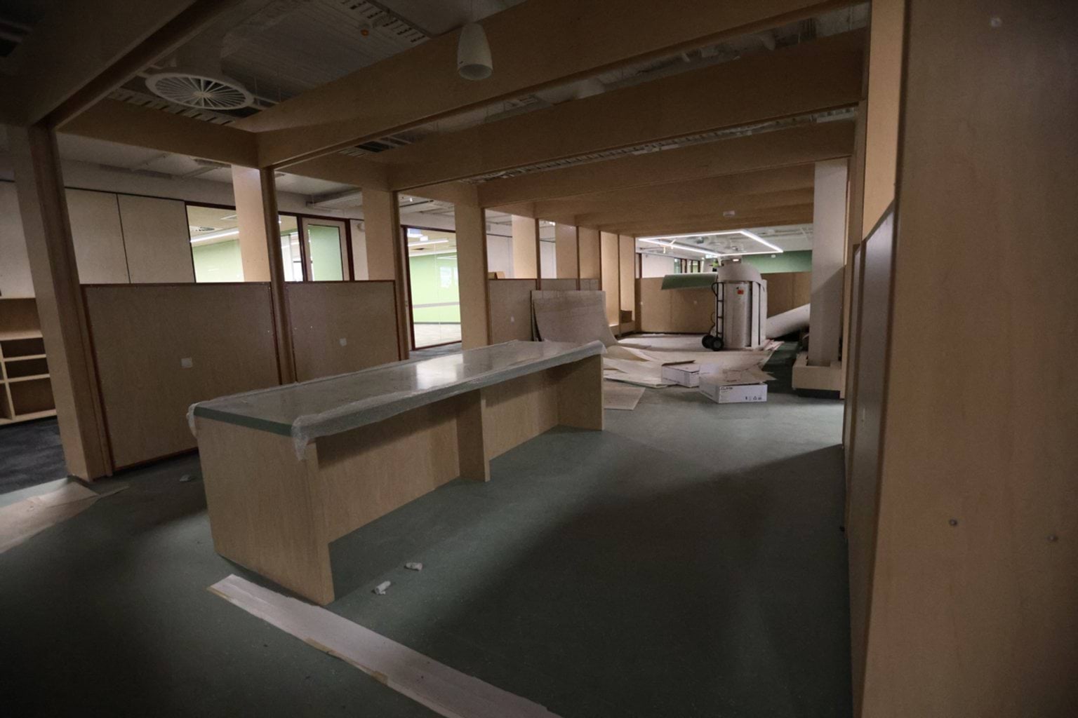 School room under construction. There is a bench in the middle of the room, wooden walls along the outside, and a view of the hallway.