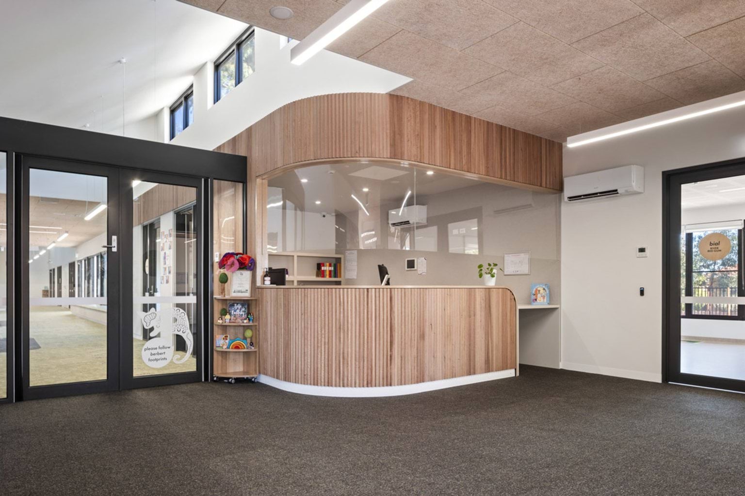 Reception area with curved timber feature desk, glass doors and bright interior with overhead lighting