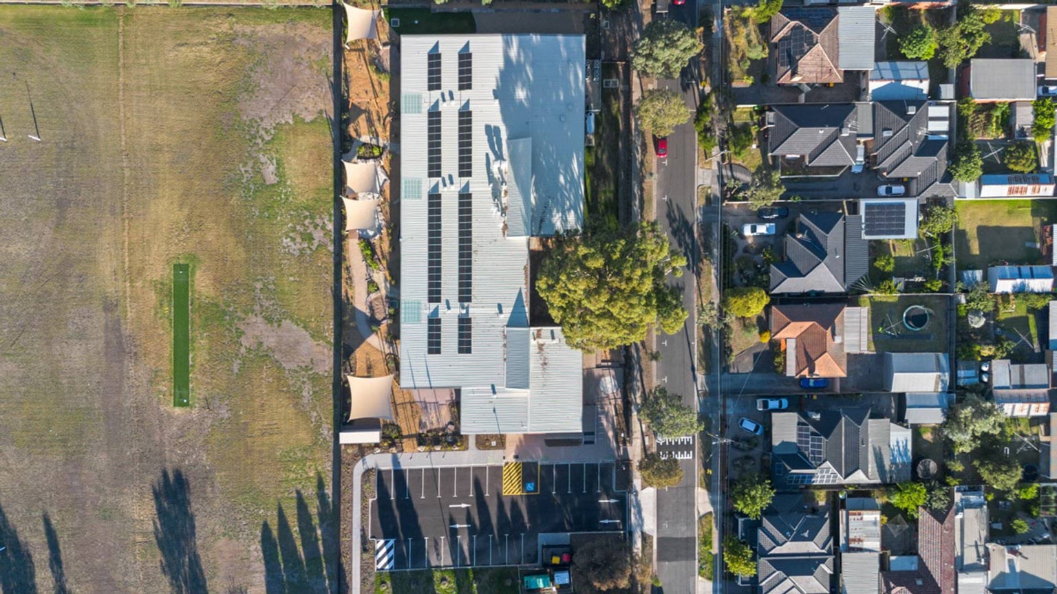 Top-down view of a building with solar panels, adjacent car park and surrounding residential streets