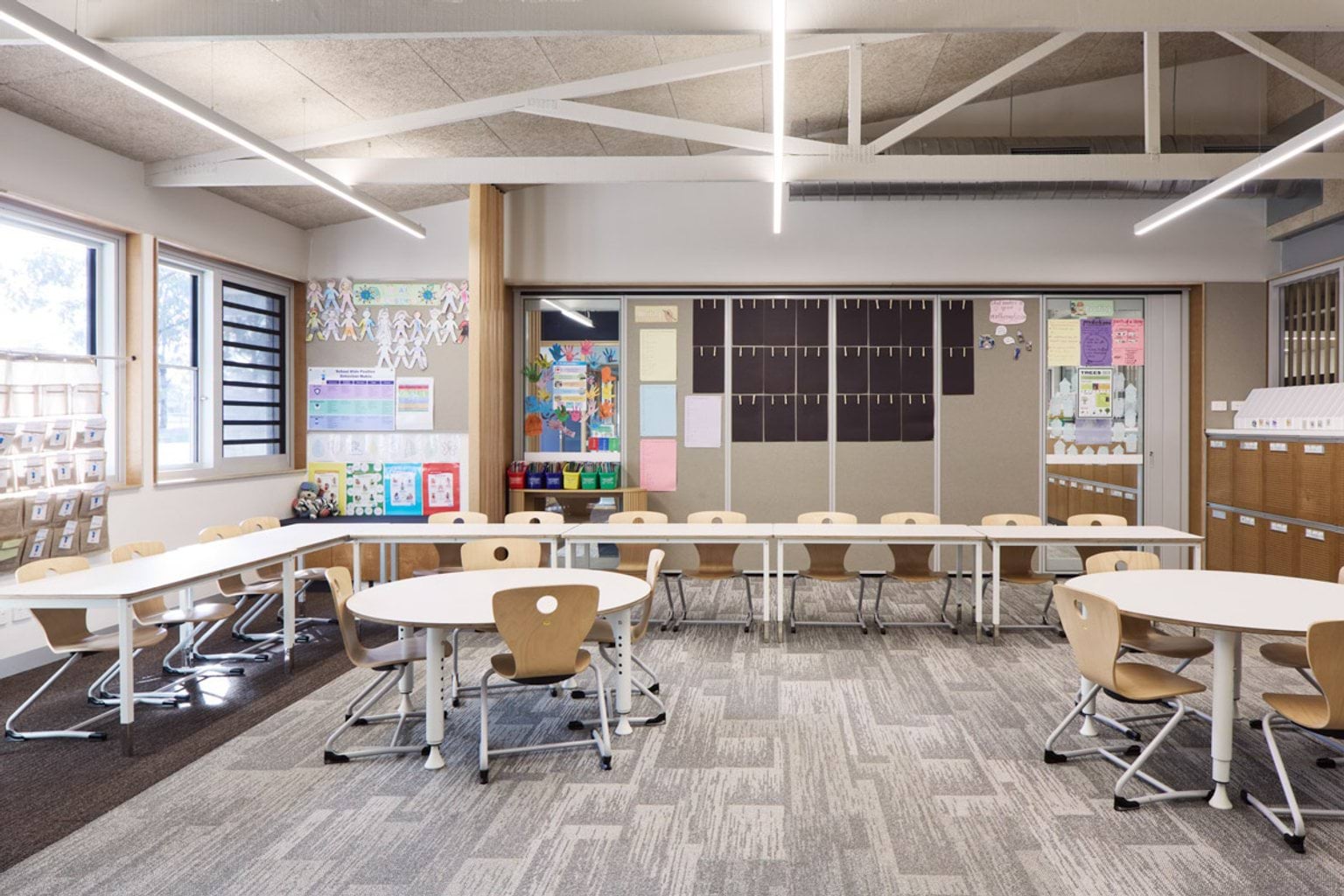 A classroom with round tables and timber chairs. Colorful student work is displayed on the walls.