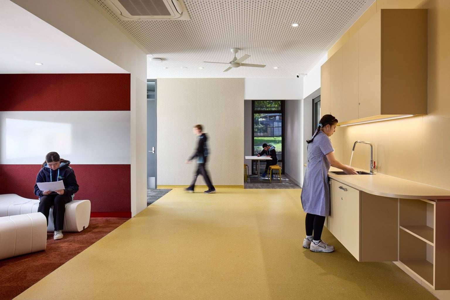 A classroom with white tables and blue chairs. A red arched alcove creates a reading nook, and colourful decorations hang on the walls.
