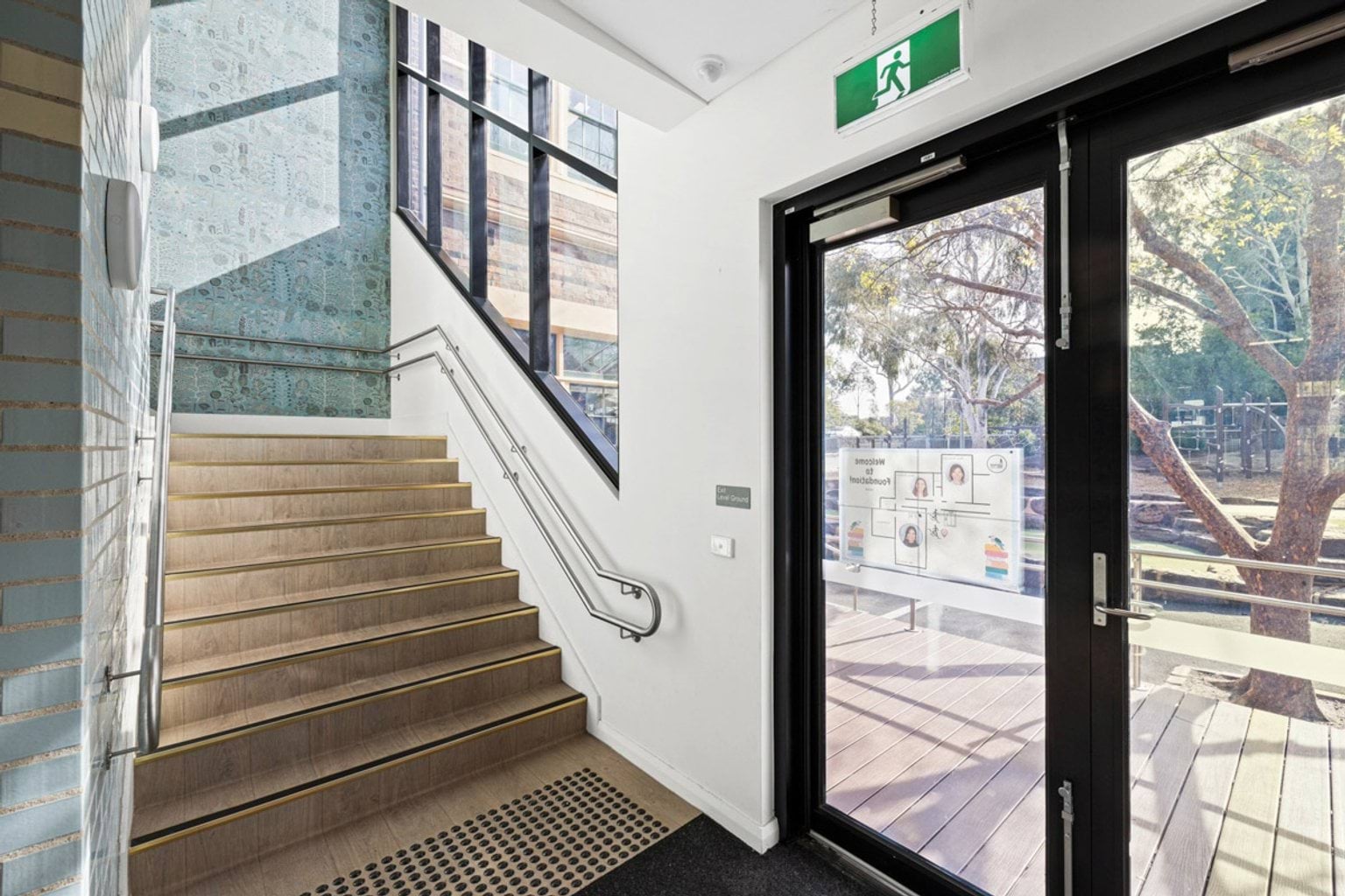 A staircase with timber steps and metal handrails next to glass exit doors opening to a timber deck outside.
