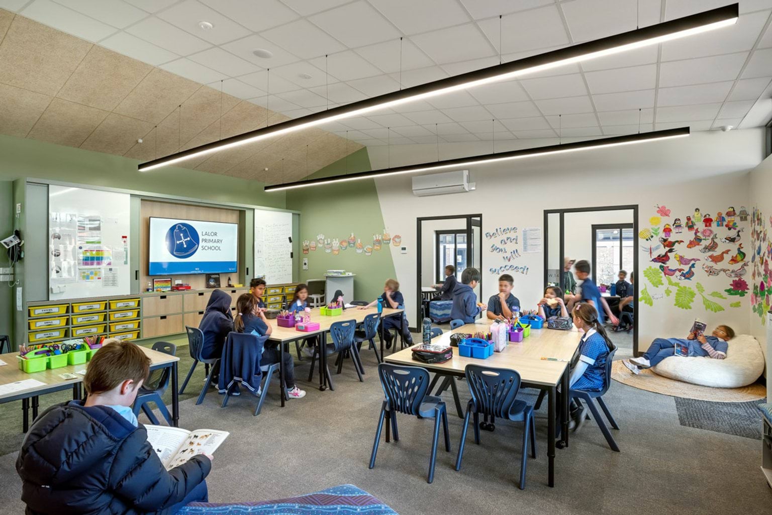 A classroom with green walls, large tables, and an interactive screen displaying “Lalor Primary School.” Student artwork decorates the walls.