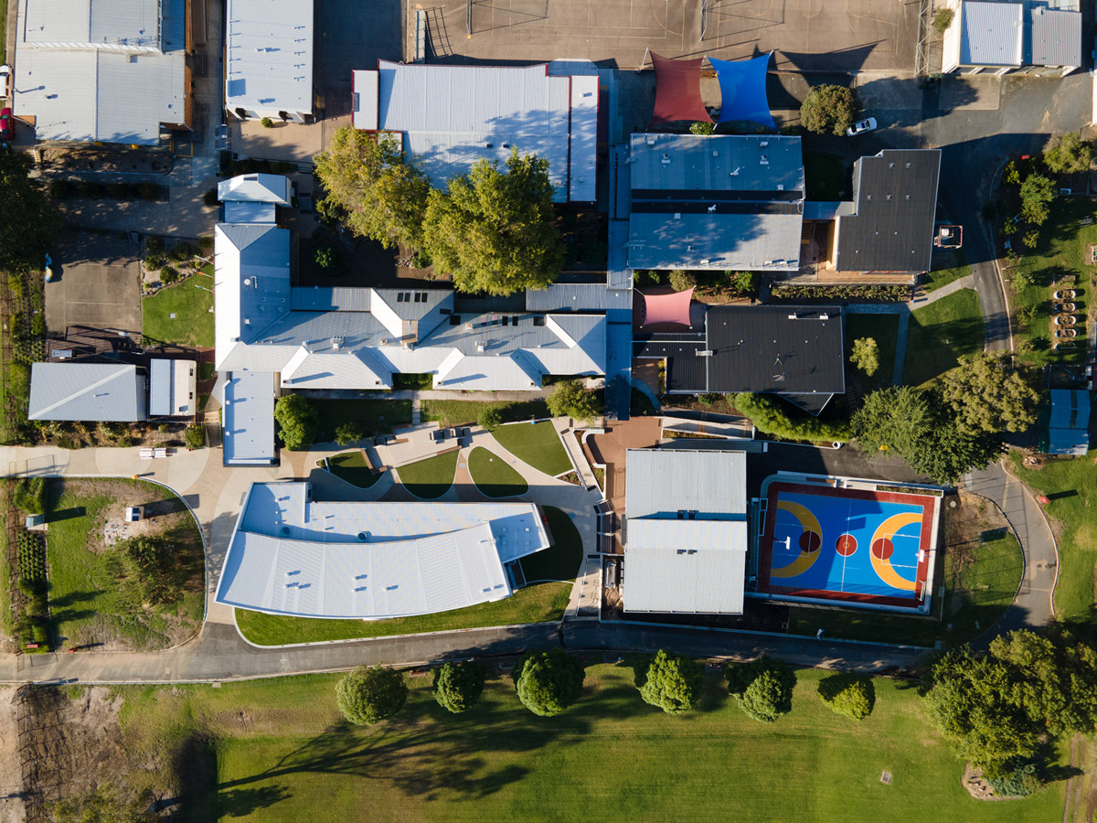 Aerial view of school campus showing multiple buildings, landscaped areas and a colourful outdoor sports court