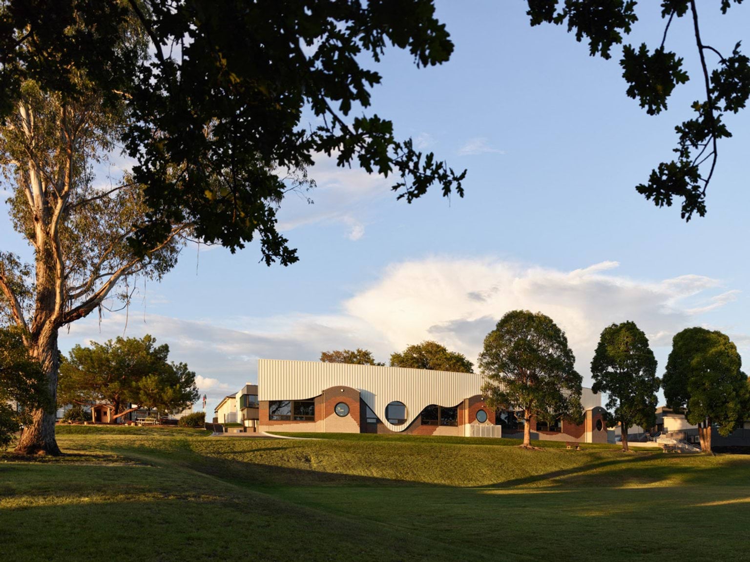 School building with distinctive curved design and circular windows, set on landscaped grounds with large trees