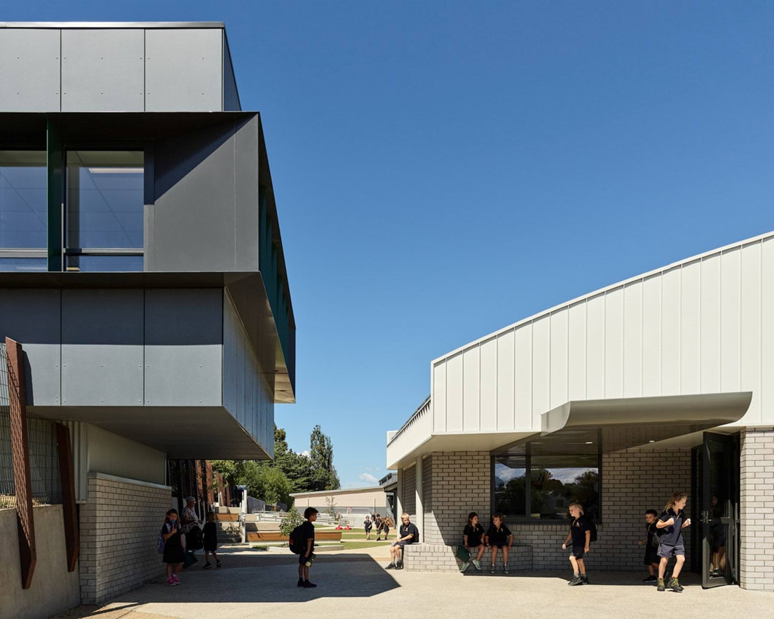 Outdoor walkway between two modern school buildings with students gathered and walking through open space