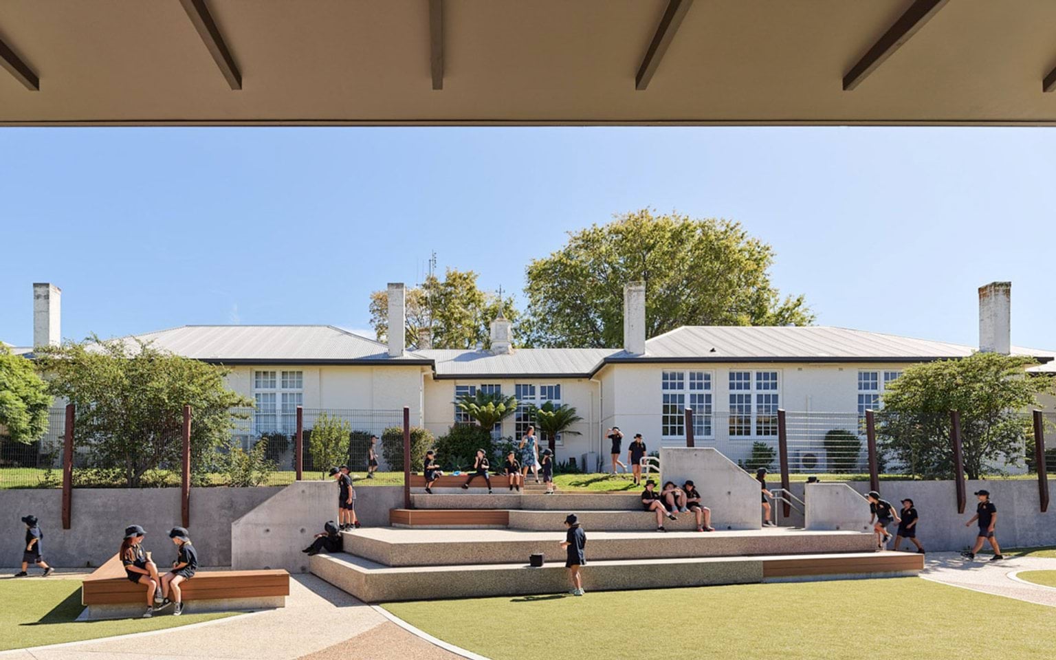 Outdoor courtyard with tiered seating and landscaped area in front of a school building, students sitting and walking