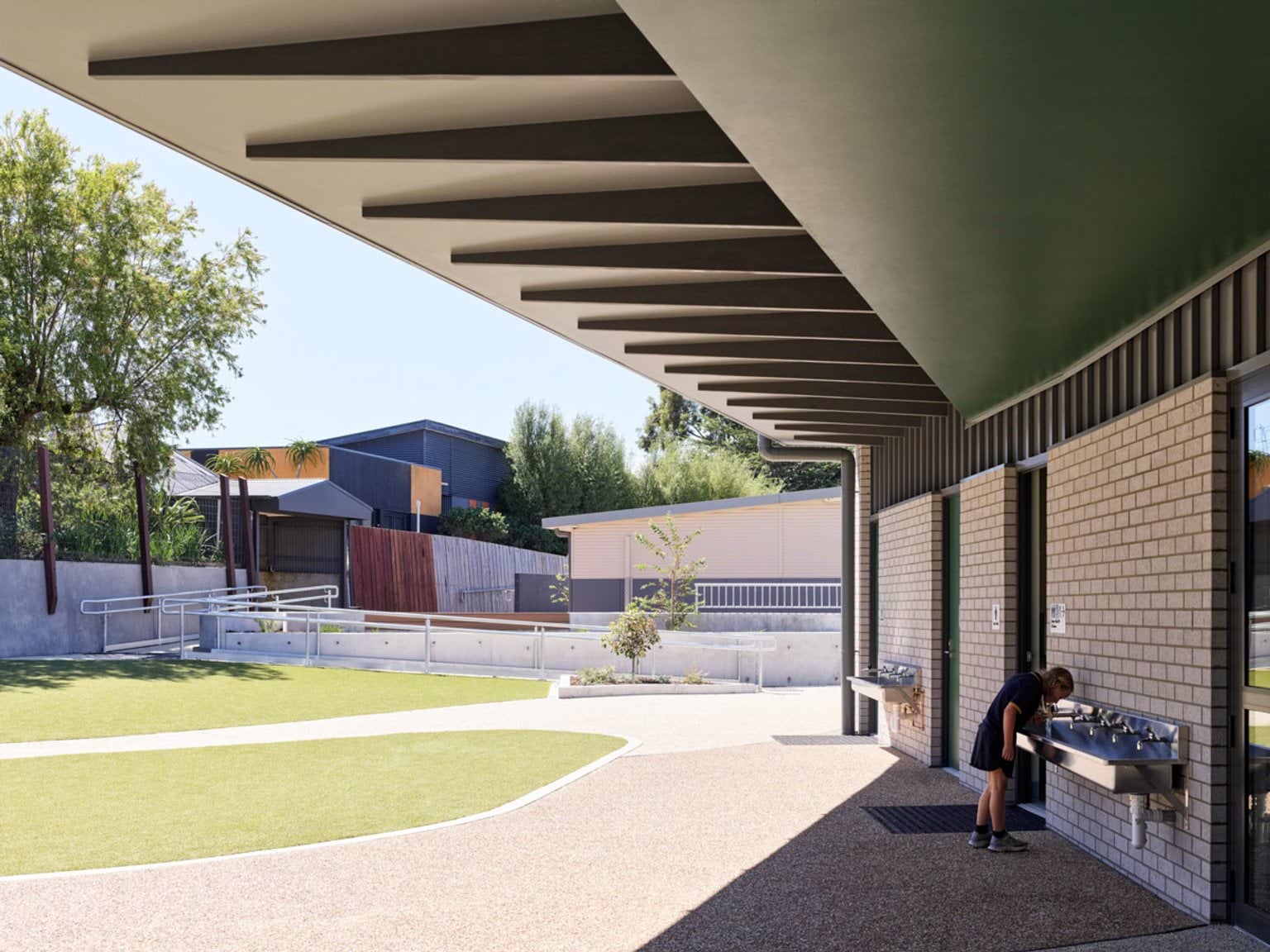Covered walkway with angled roof beams and brick wall, student drinking from water fountain