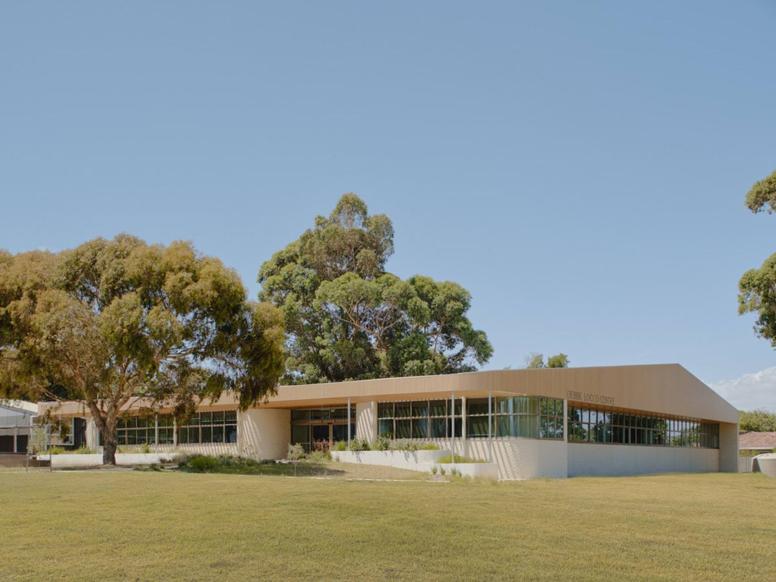 The exterior of a new centre, a modern school building with a light timber facade and large windows. It is surrounded by grassed areas and mature trees.
