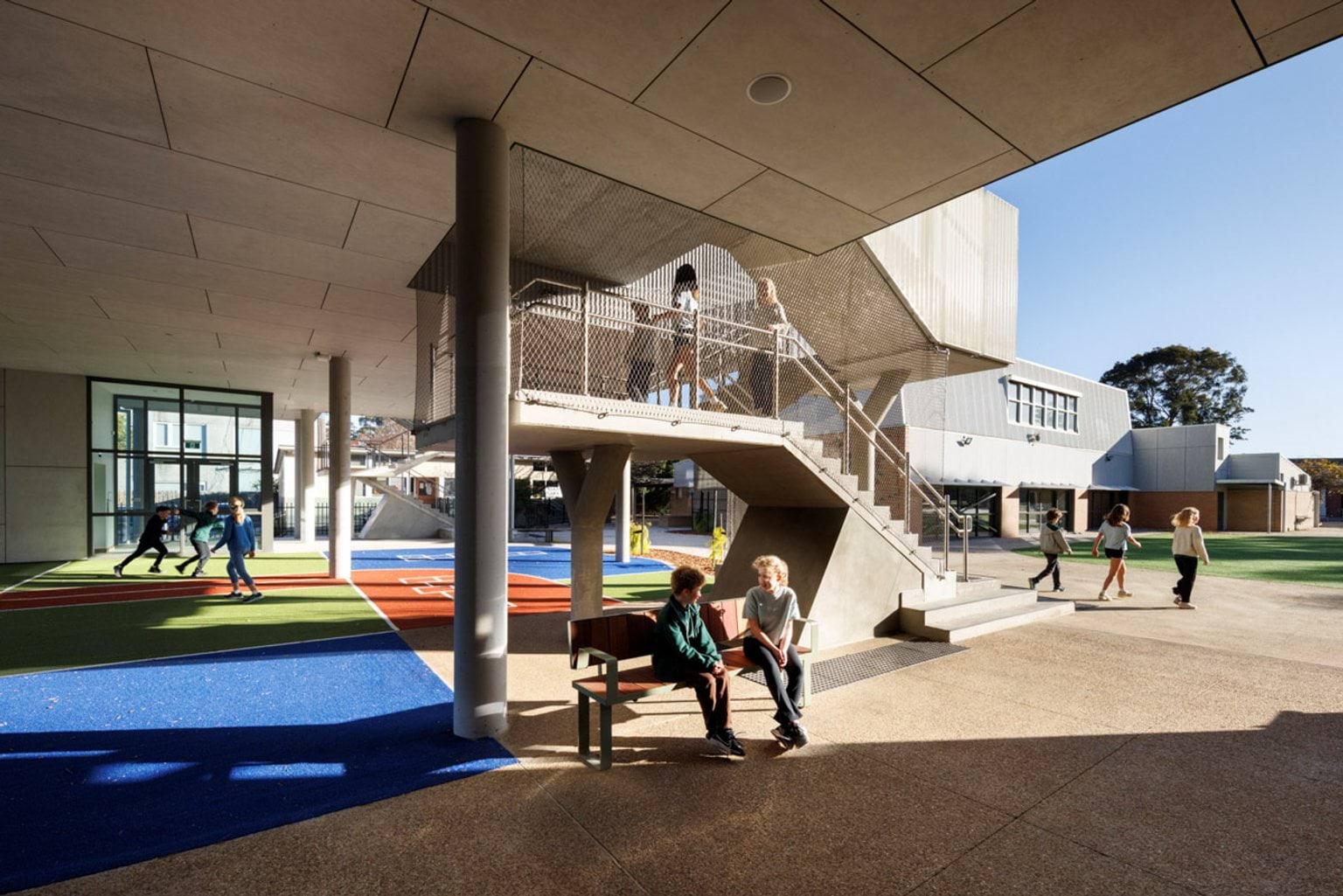 A covered outdoor play area with colourful synthetic turf and a staircase leading to the upper level of the school building.
