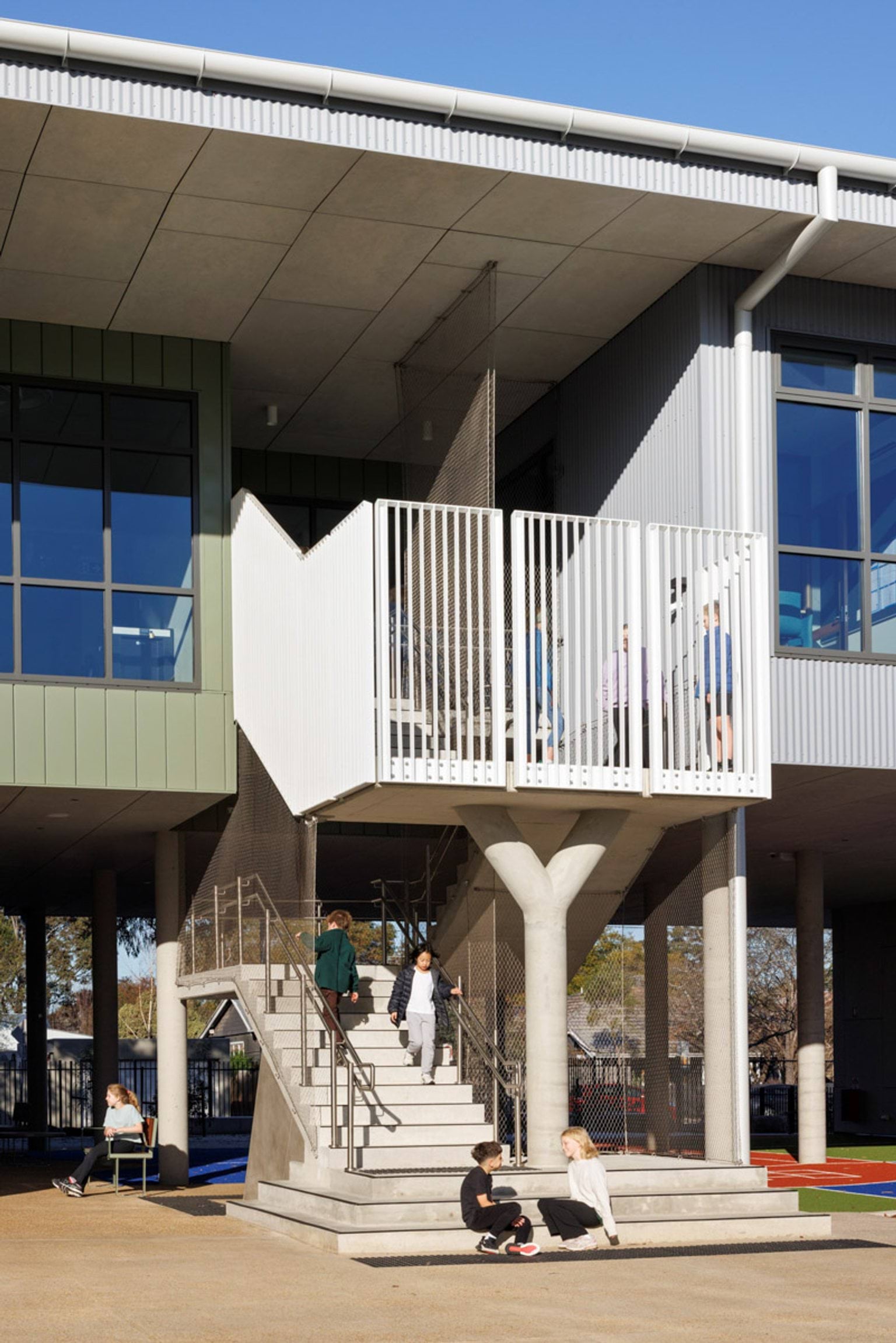 Concrete stairs with metal railings leading to an upper level of the school building. Students are sitting and walking nearby.