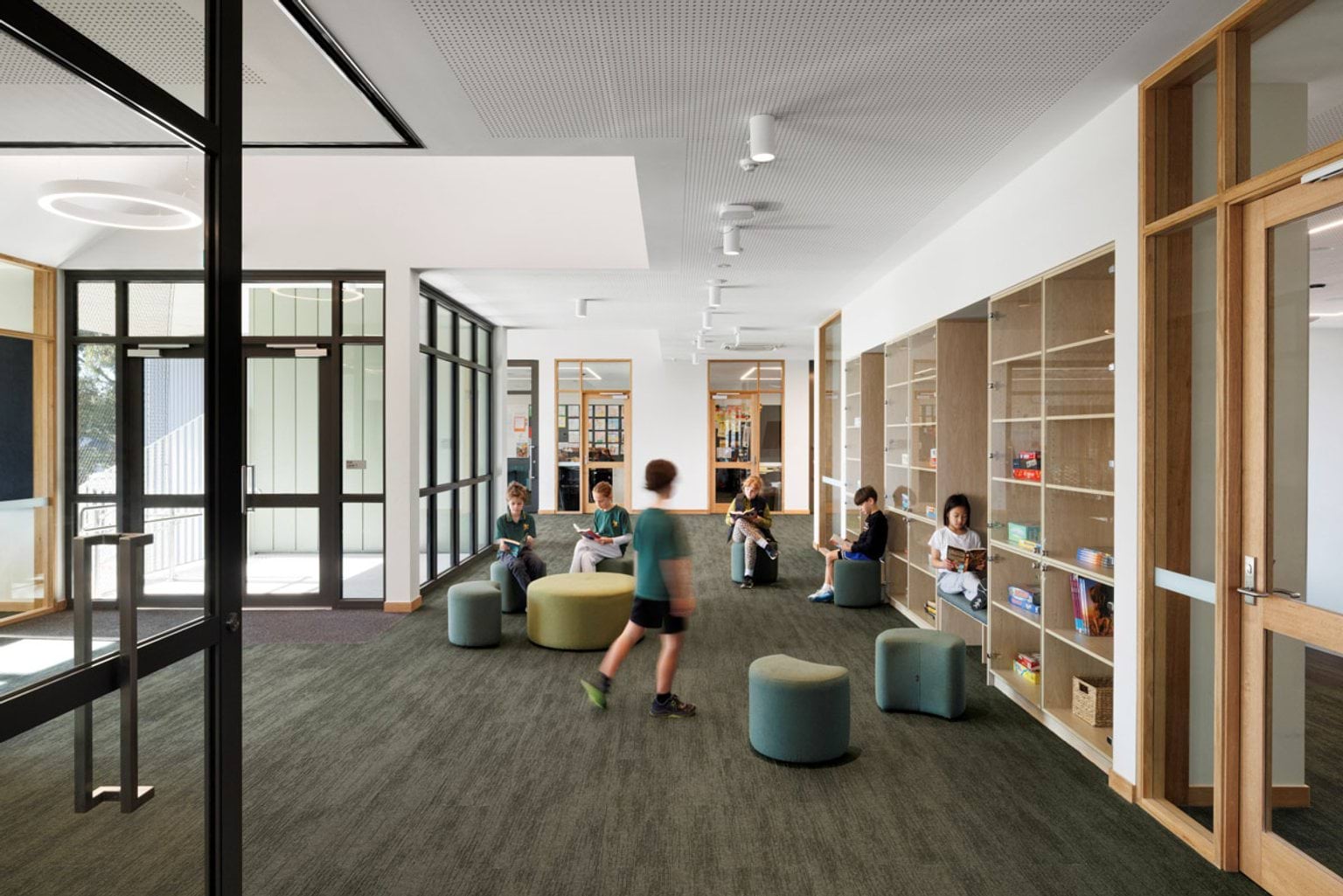 A breakout area with cushioned stools, built-in shelving, and glass doors. Students are reading and working in the space.