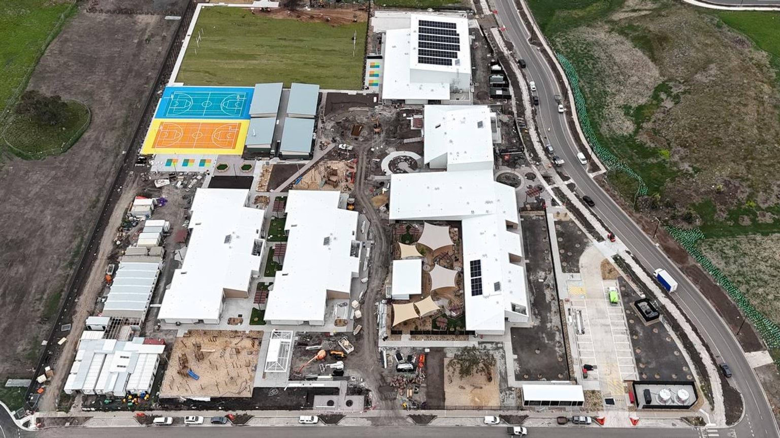 Aerial photo of school under construction with multiple buildings, play areas, and sports courts