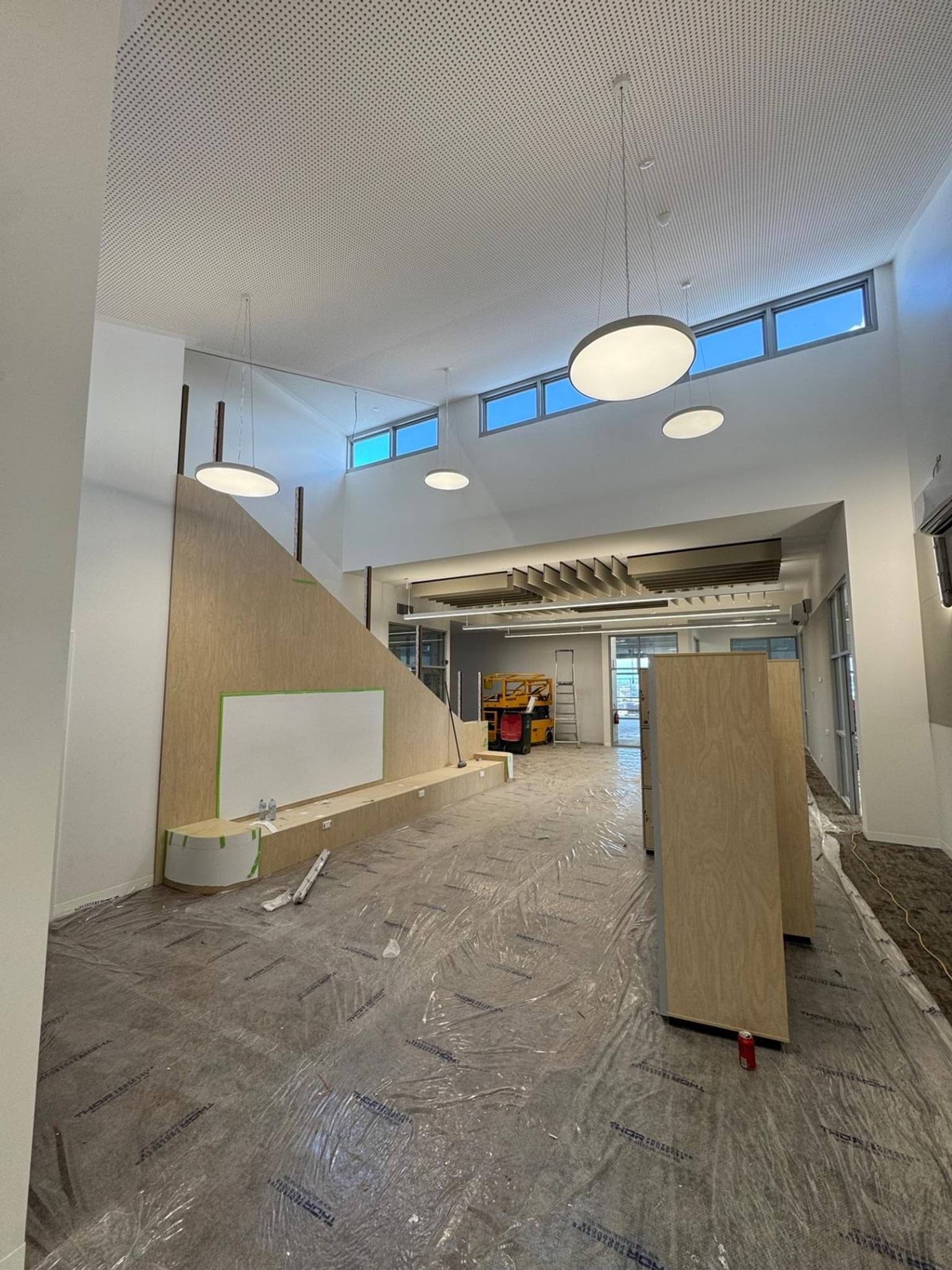 Inside of school hall with seating, white board, and high ceiling with windows