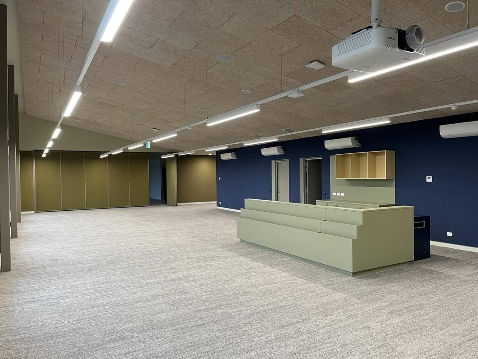 Inside school room. There is a projector on the ceiling, main desk, and air conditioning units