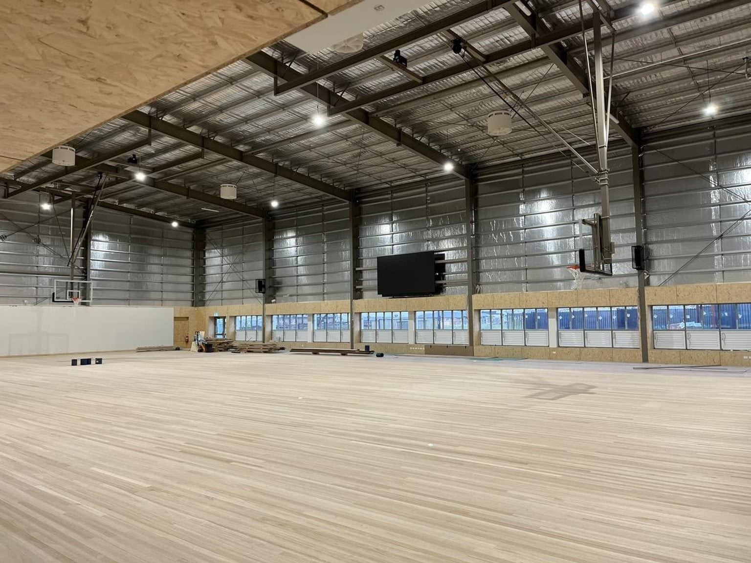 Indoor gym. There are basketball hoops and a court under construction.