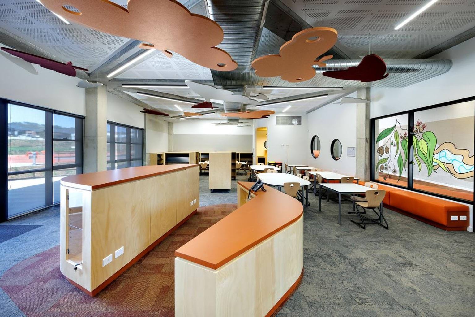 Inside Kerribana Primary School. The room has multiple orange butterfly designs suspended from the ceiling. There are long benches in the middle of the room with orange countertops and desks with chairs also in the room.