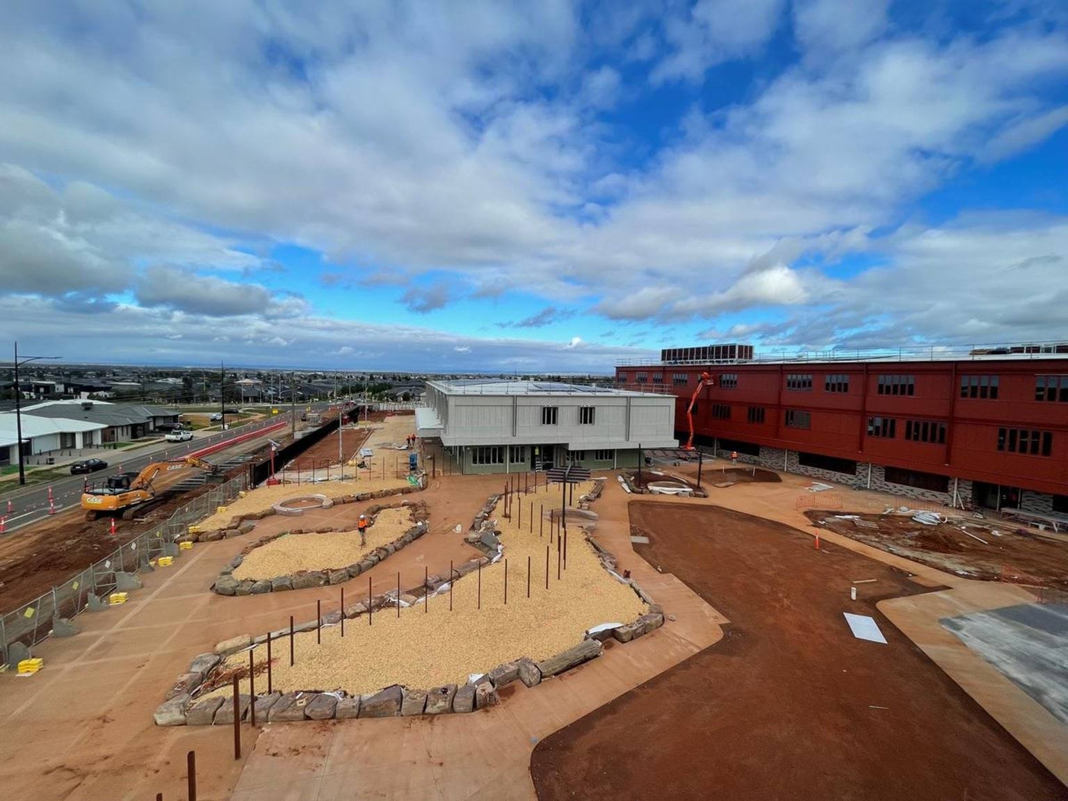 Aerial view of school grounds under construction. There is soil and scaffolding in the foreground, with multi-level school buildings in the background.