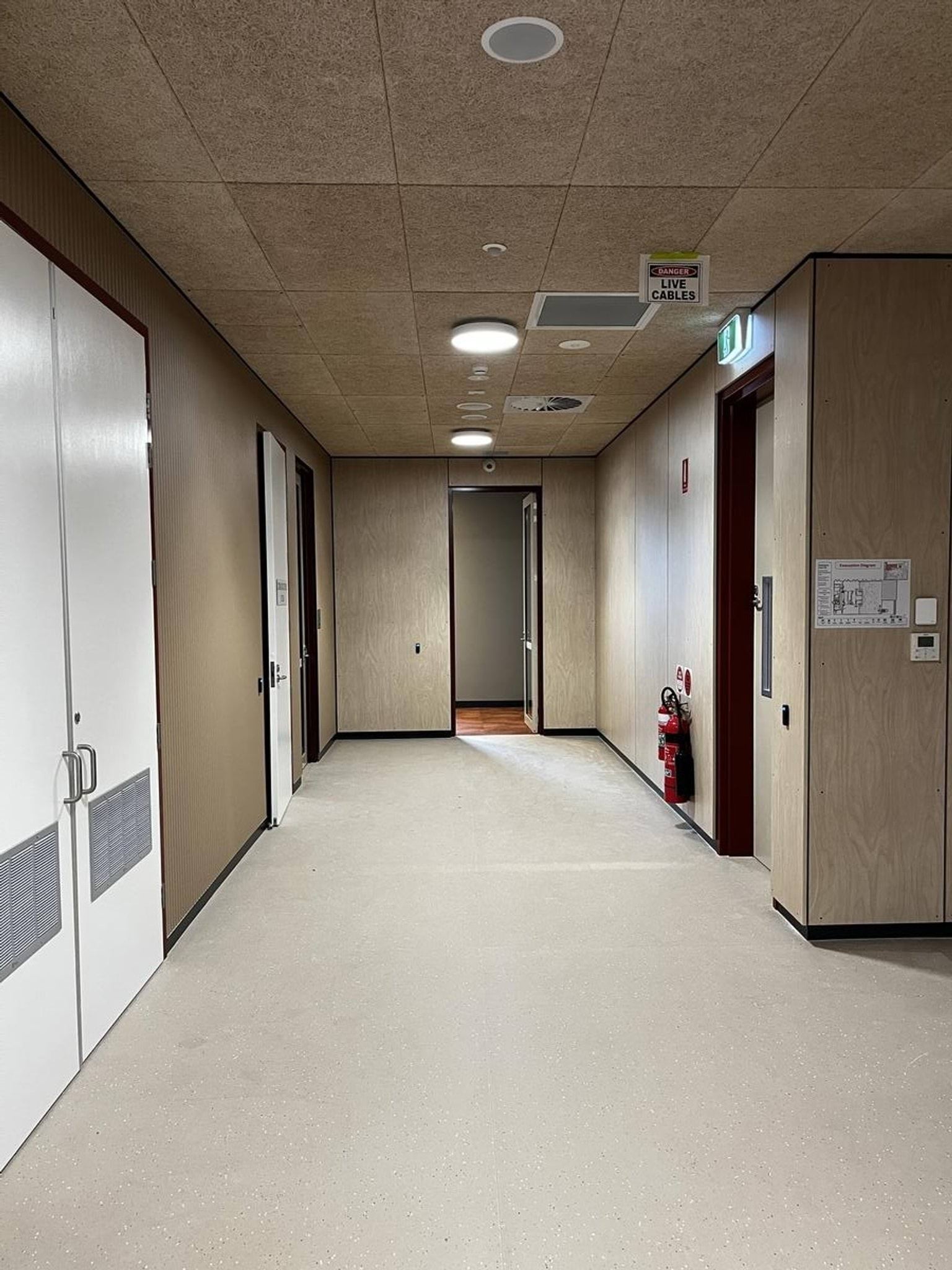 A simple hallway with timber wall panels, light flooring, and ceiling lights, leading to multiple rooms.