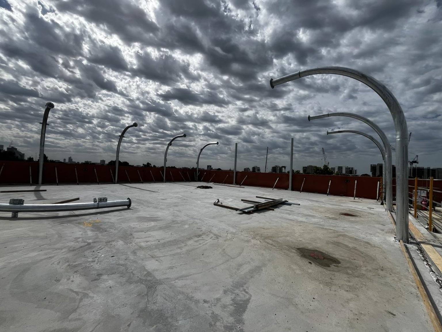 A bare concrete rooftop with curved metal frames installed along the edges under a dramatic cloudy sky.