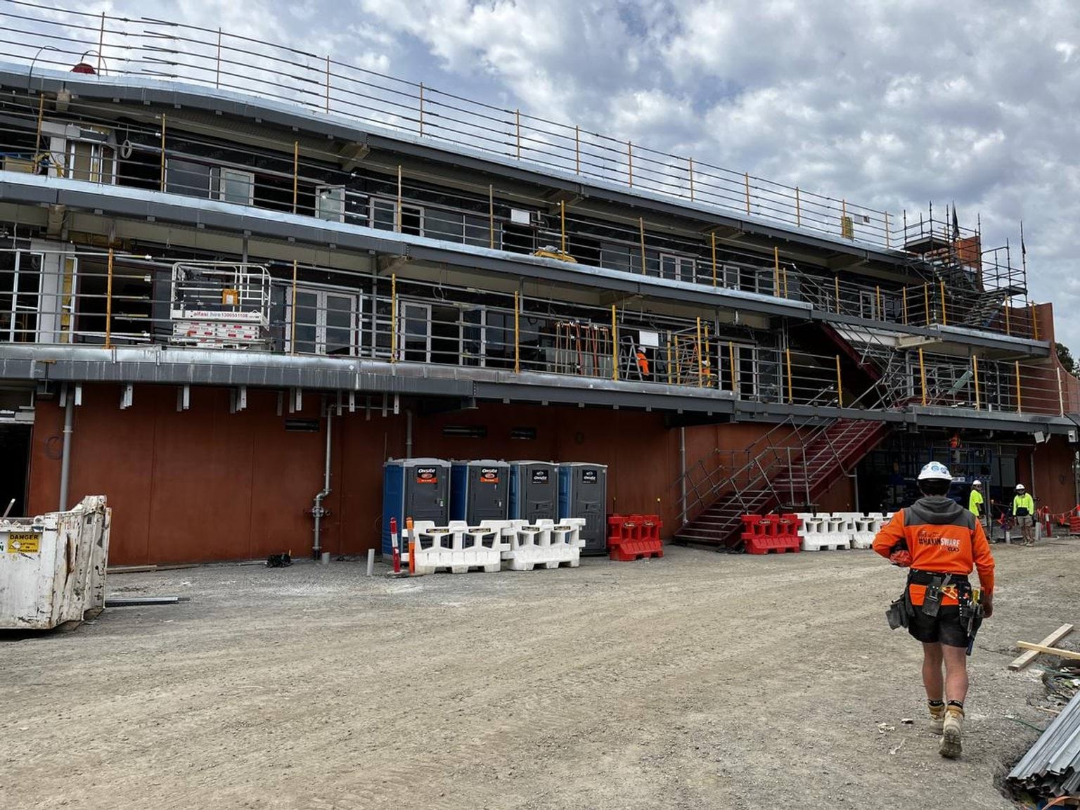 The exterior of a multi-level school building under construction with scaffolding, safety barriers, and portable site facilities.