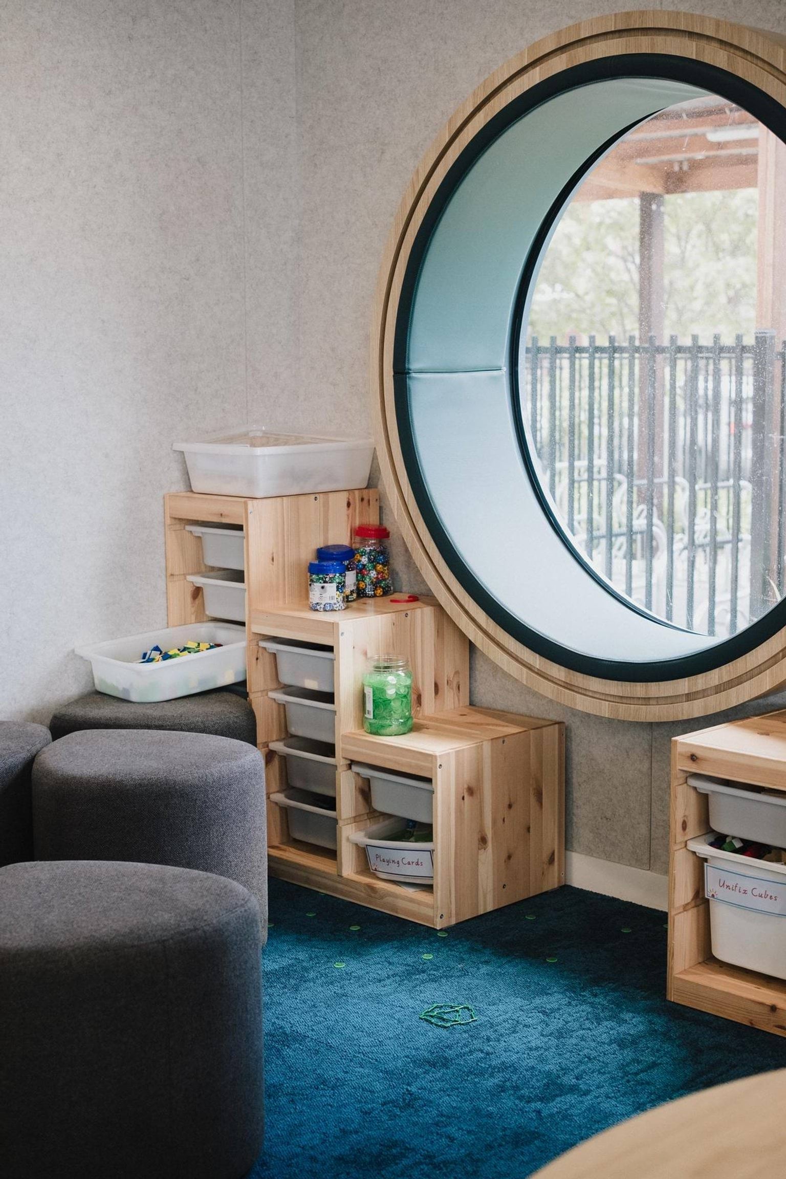 Indoor play area with timber storage units and a large circular window providing natural light