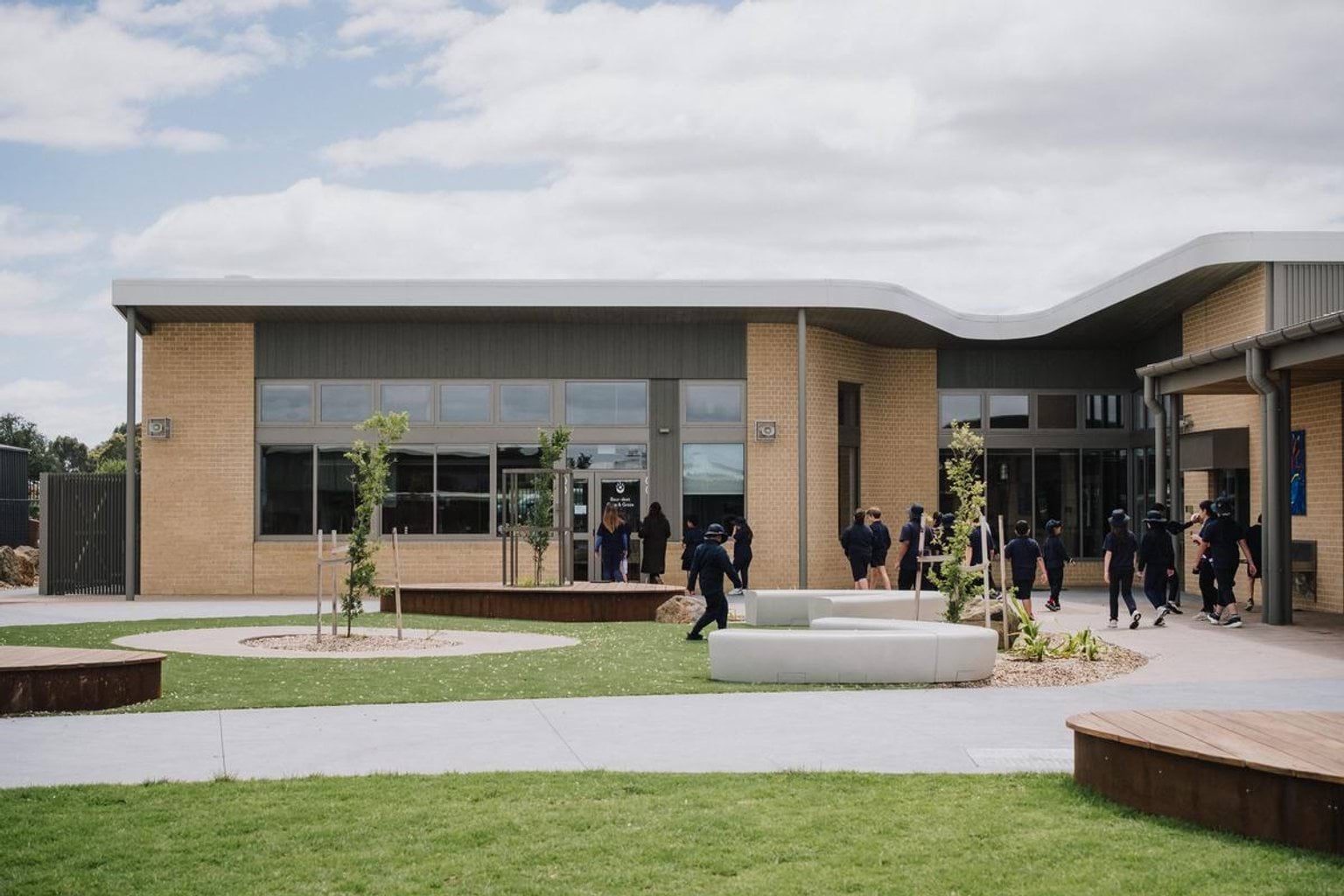 Single-storey school building with brick and metal cladding, landscaped courtyard and students walking outside