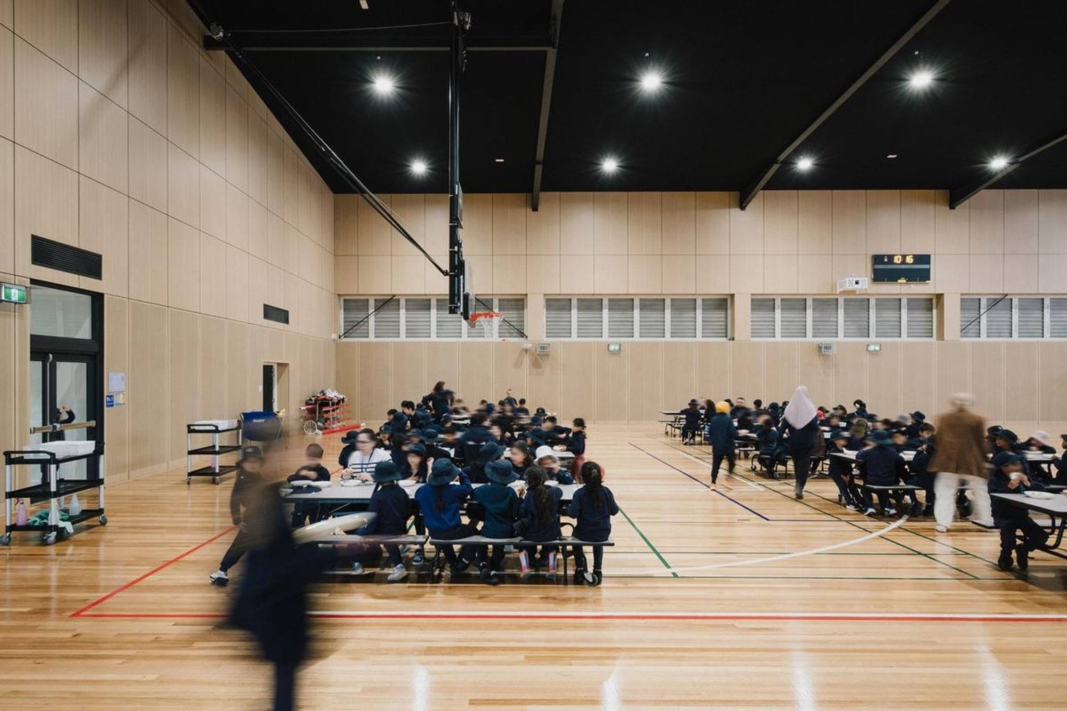 Indoor sports hall with timber flooring and high ceiling, with students seated at tables for an activity